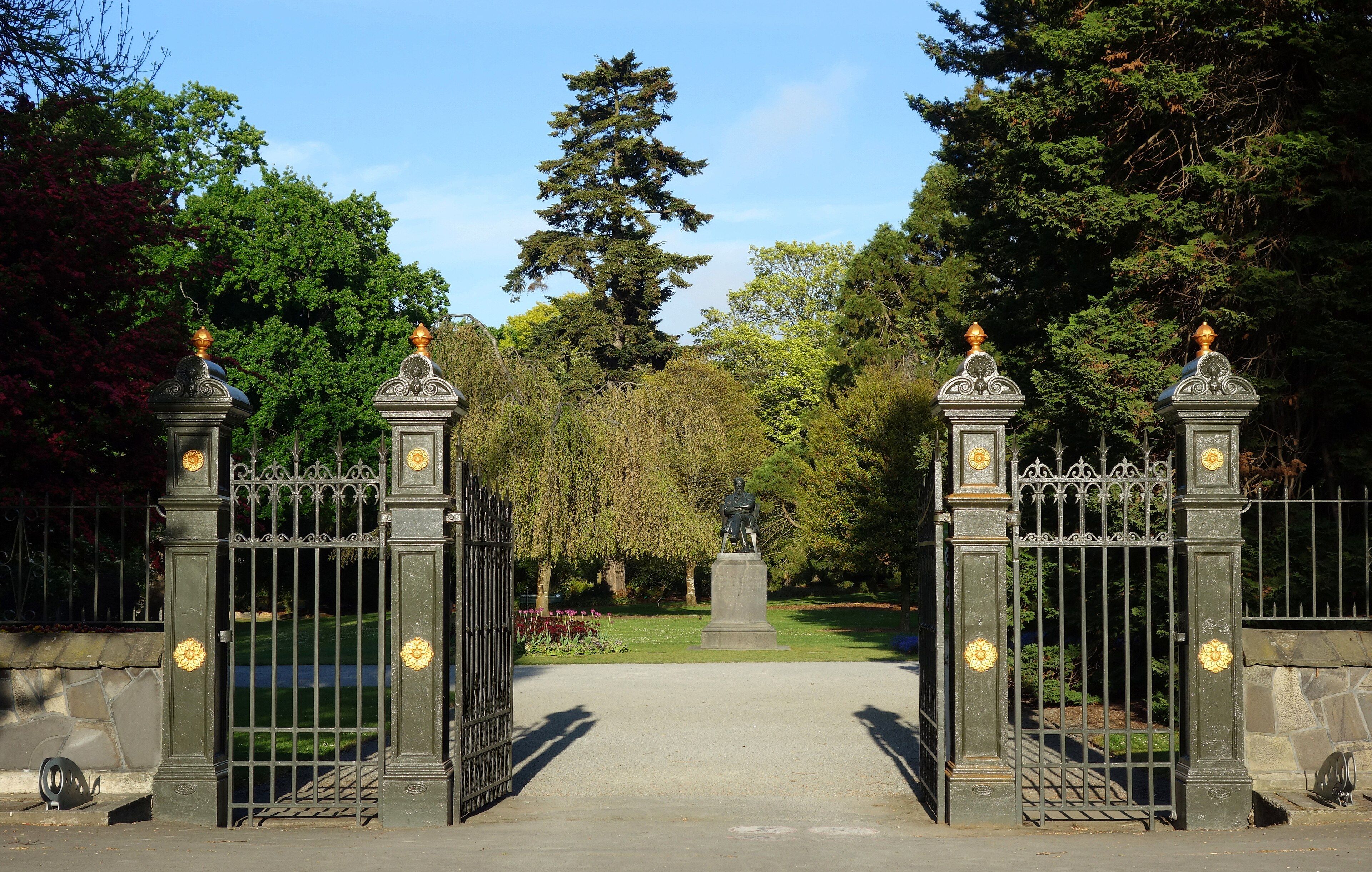 The iron gates and stone piers at the entrance to Christchurch Botanic Gardens, with tall trees behind.