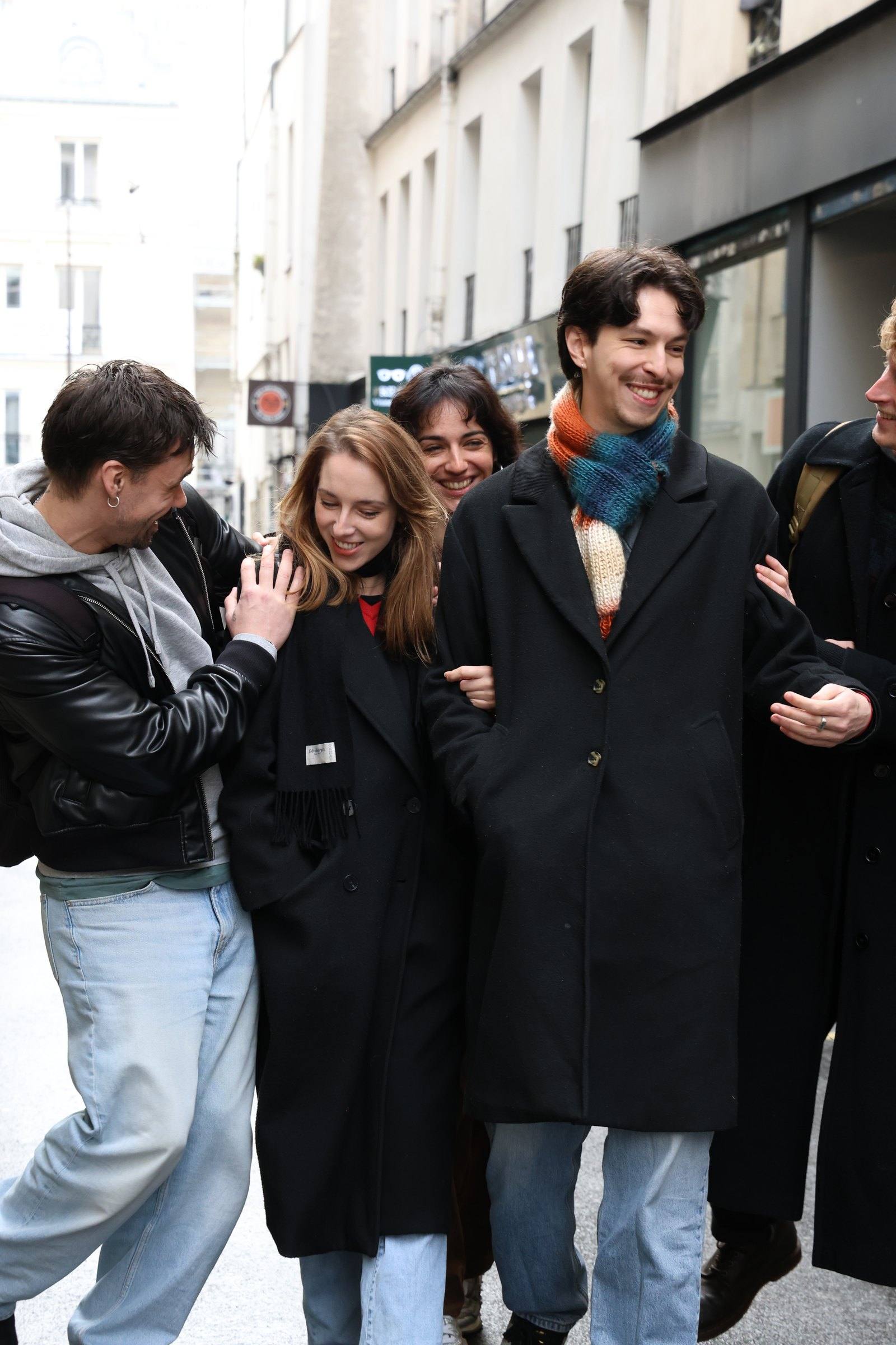 Six friends laughing as they walk arm in arm down a narrow street on a Timeleft walk