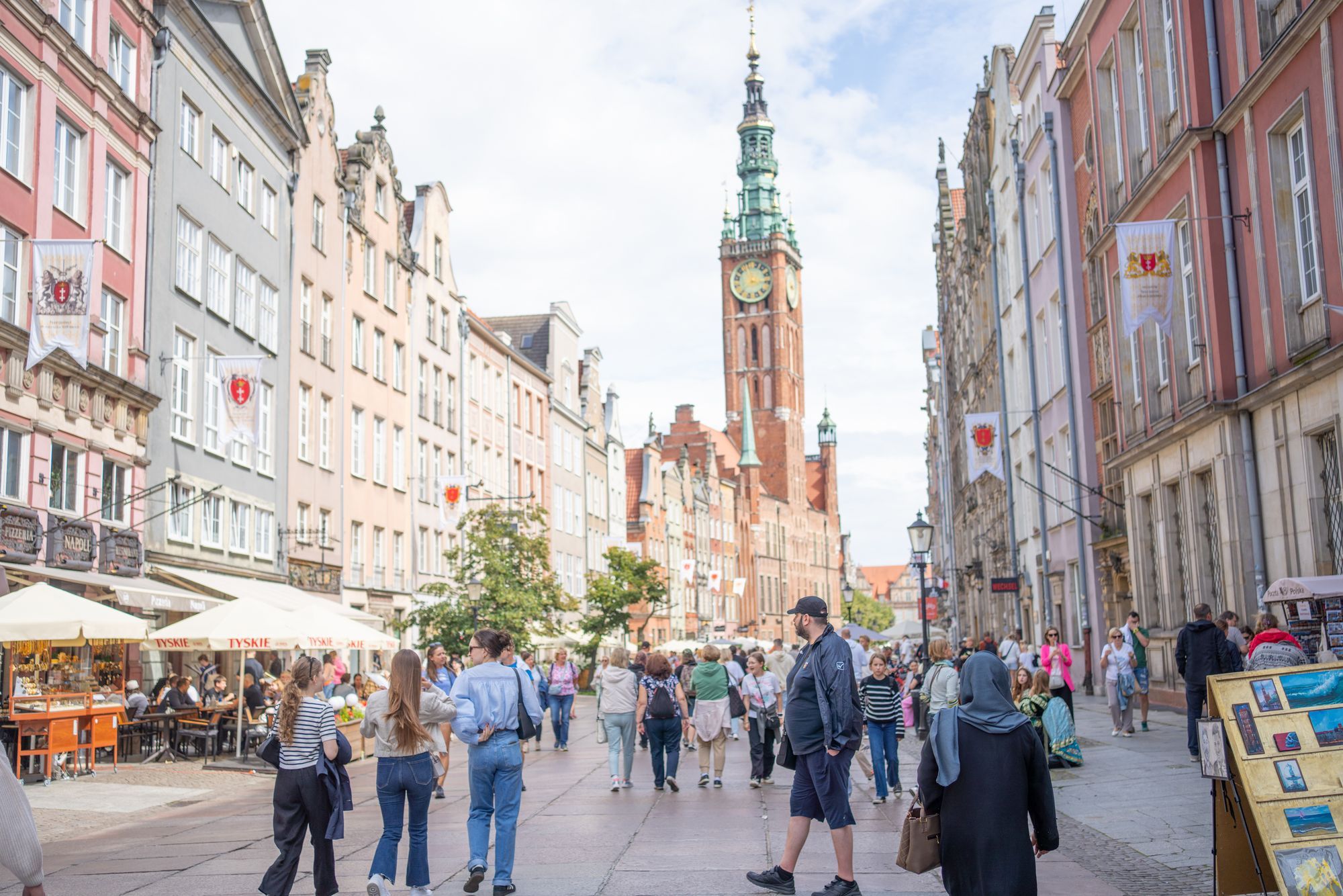 Visitors walking along Long Market in Gdańsk with cafe tables on the left and the Main Town Hall tower ahead.