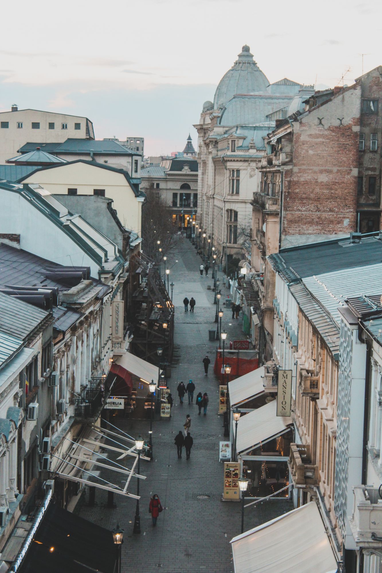 People walking along a narrow pedestrian street between old buildings in Bucharest's Old Town.