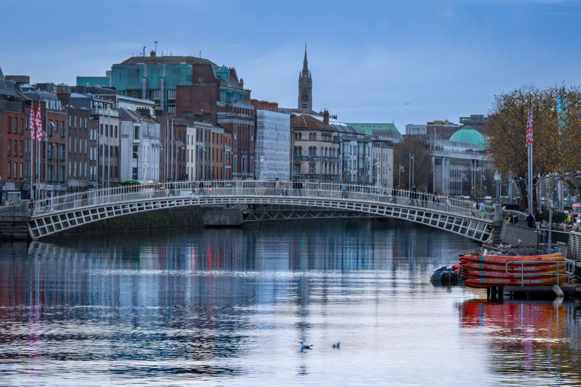 The Ha'penny Bridge and the Liffey in Dublin, with the quayside buildings and a church spire behind.