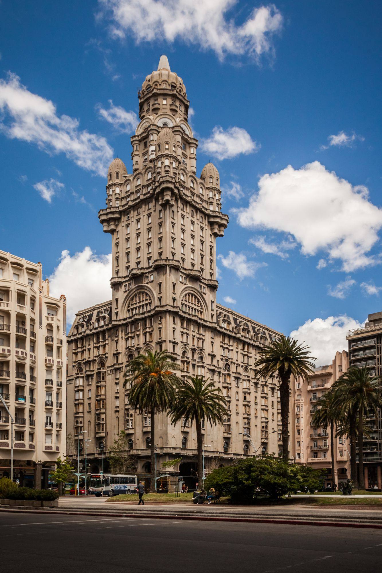Palacio Salvo rising above the palm trees near Plaza Independencia in Montevideo, under a blue sky.