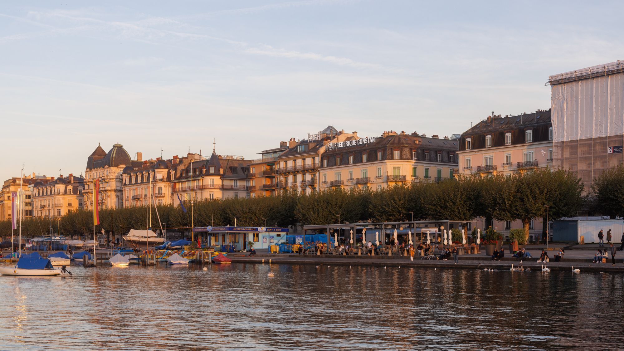 The lakeside quay and its historic buildings in Geneva at golden hour, with boats moored below.