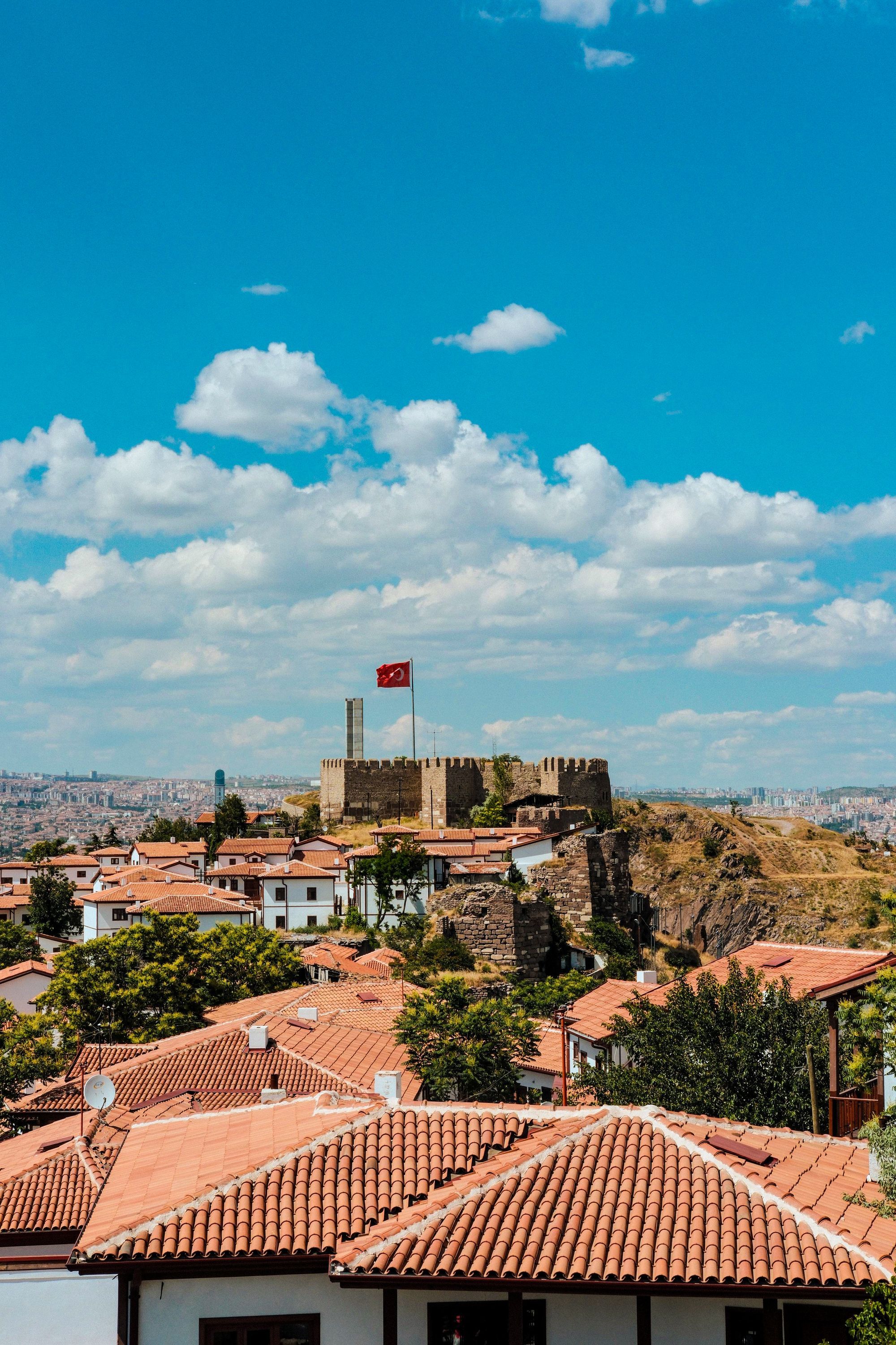 Red-roofed houses on the hillside below Ankara Castle under a sky with clouds.
