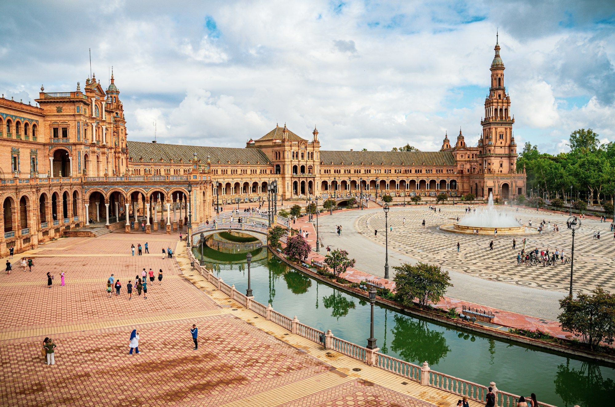 Plaza de España in Seville, with its curved brick building, a tall tower on the right and the canal and fountain in front.