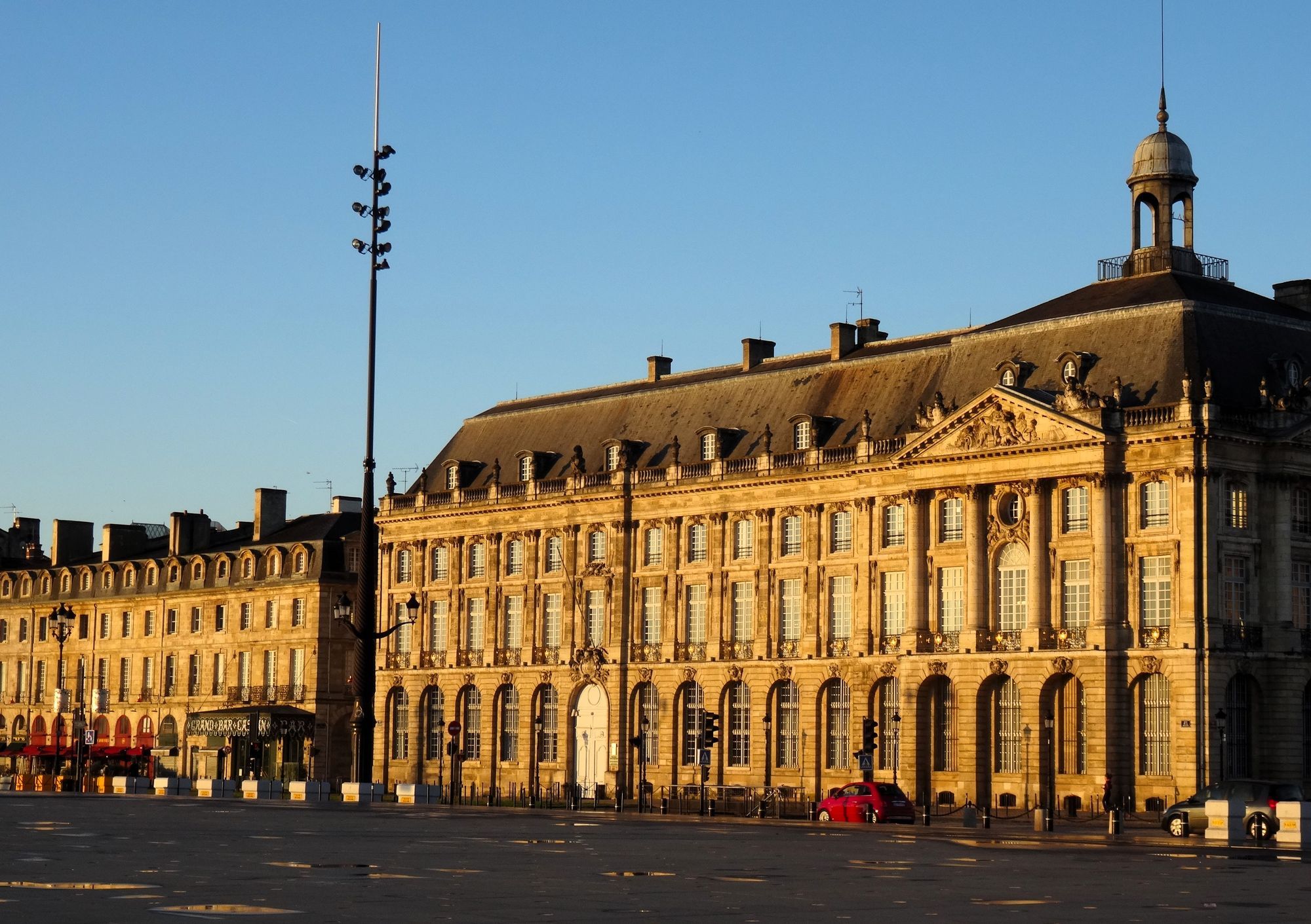 The Palais de la Bourse on Place de la Bourse in Bordeaux, lit by golden evening light under a deep blue sky.