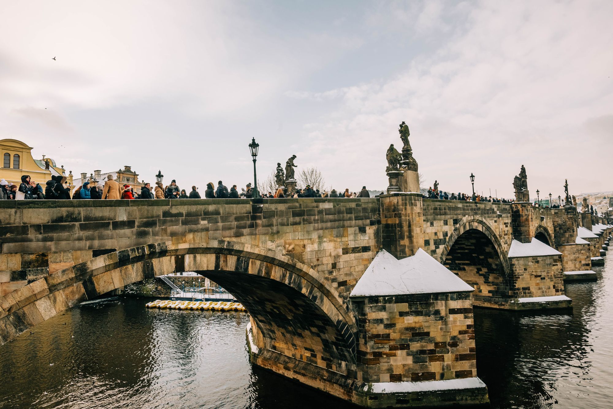 People on the Charles Bridge in Prague with the stone arches and statues.