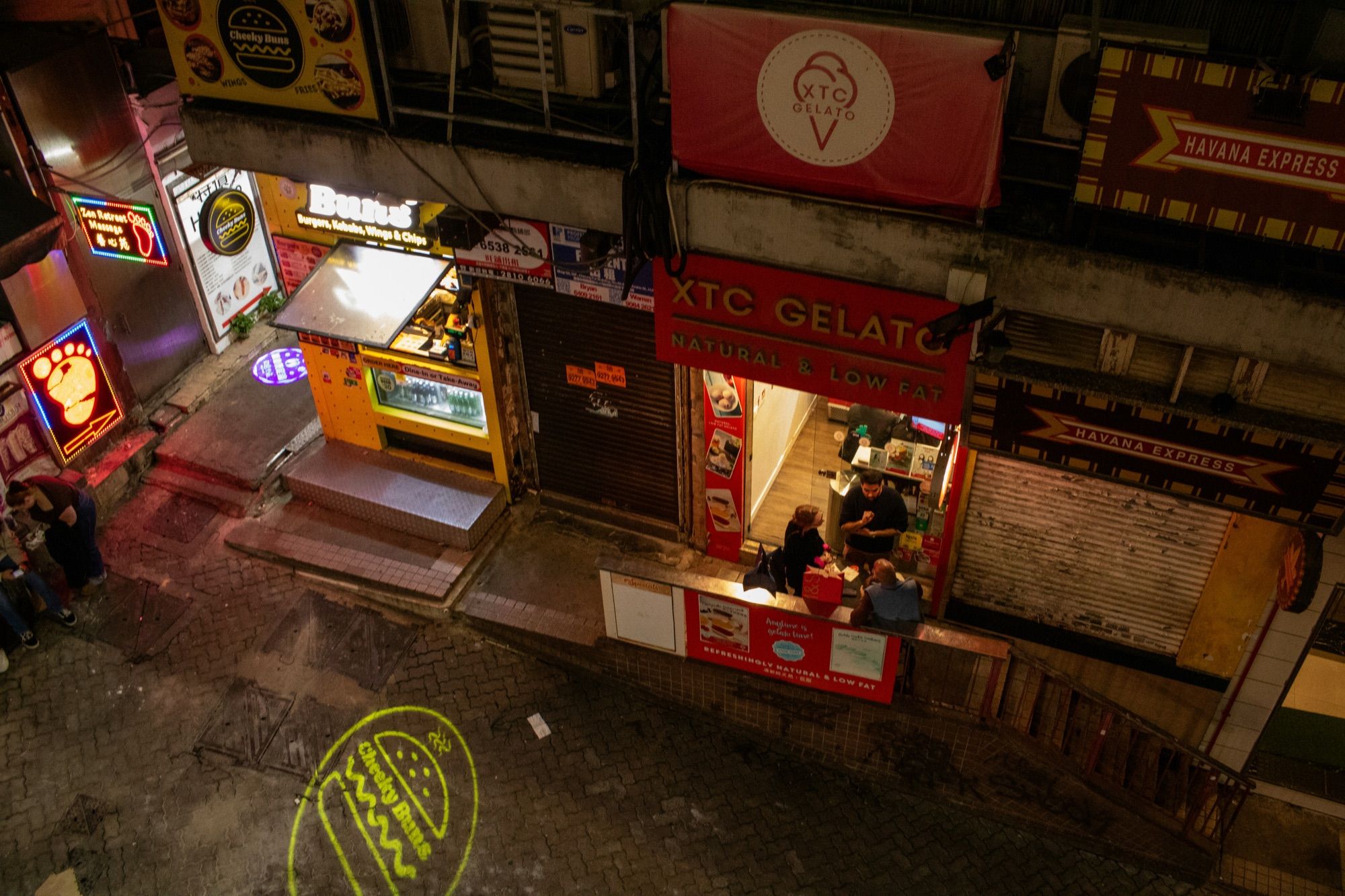 A narrow street in Central, Hong Kong, seen from above at night, with lit shopfronts