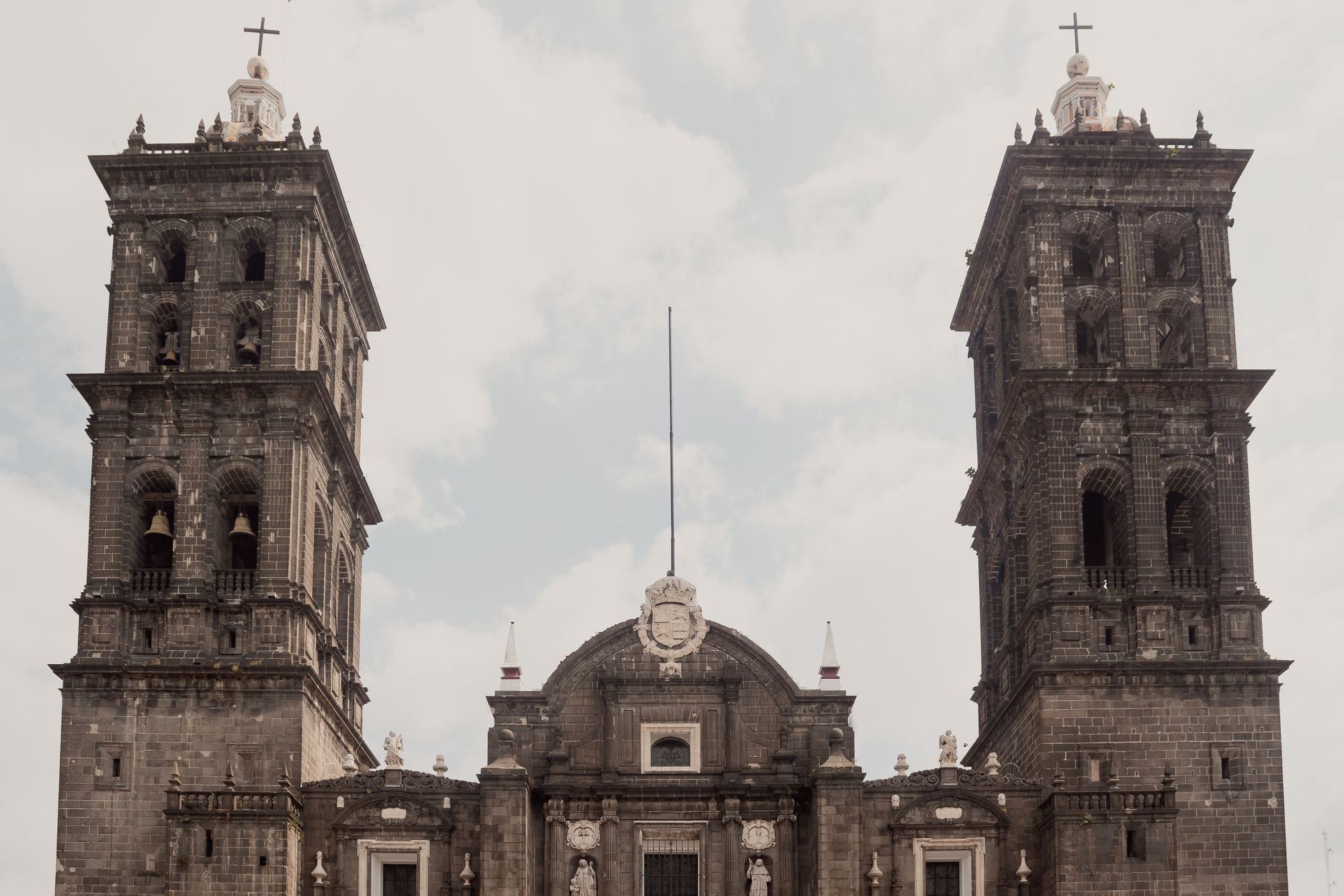 The twin bell towers of Puebla Cathedral against a cloudy sky.