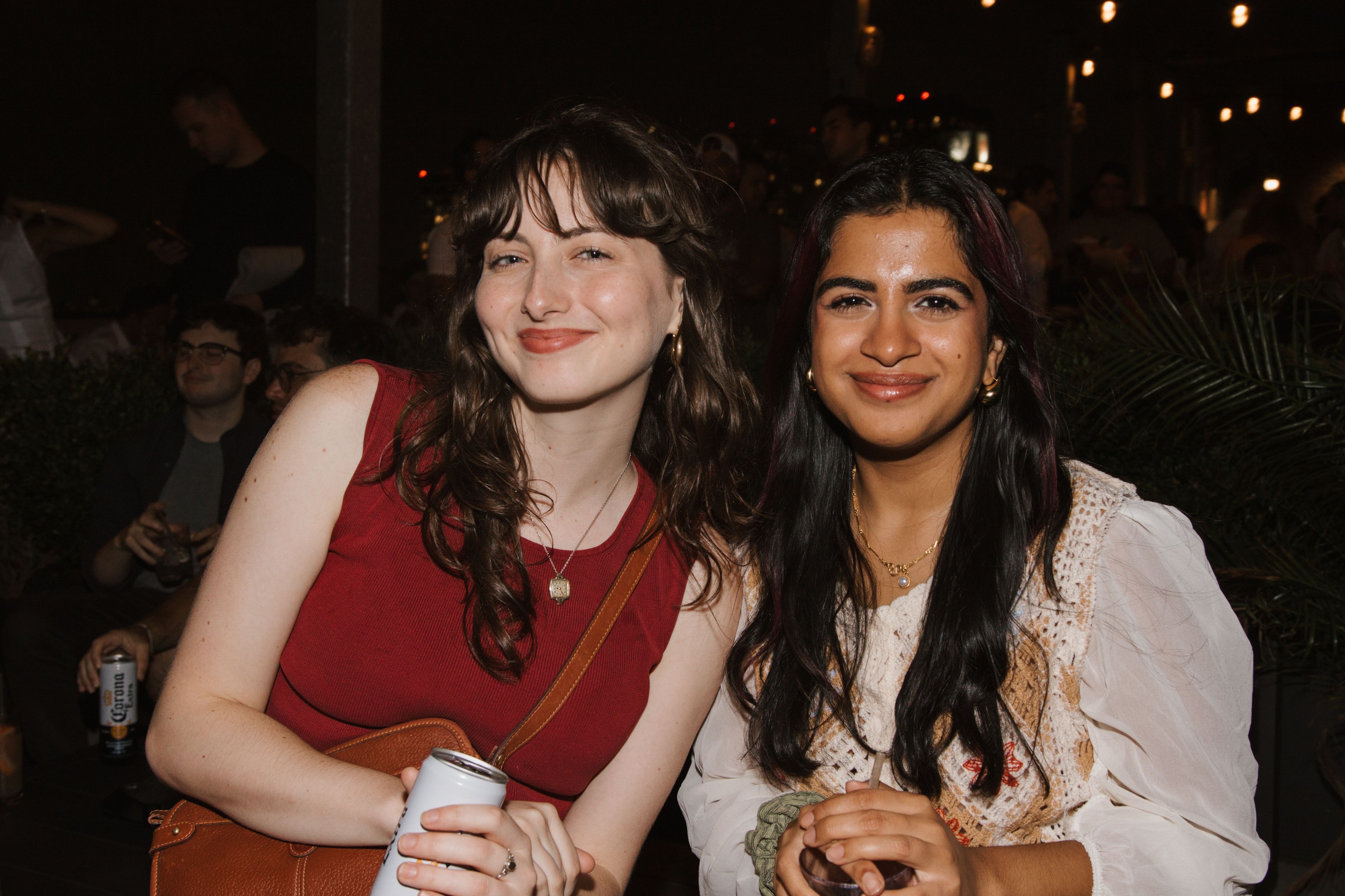 Dos mujeres sonriendo una al lado de la otra en un evento por la noche