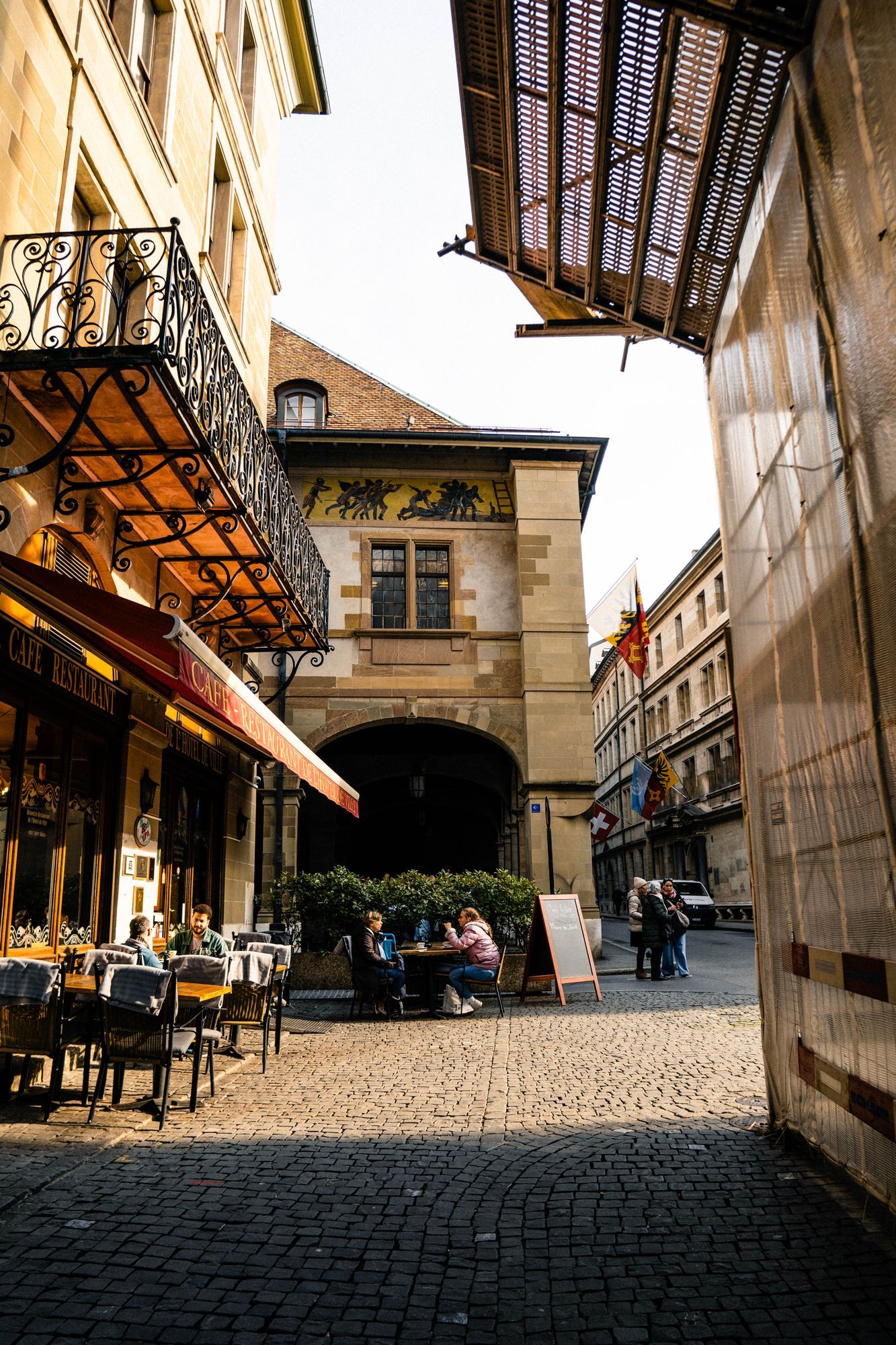 A café terrace under an archway in the old town of Geneva, with people at tables.