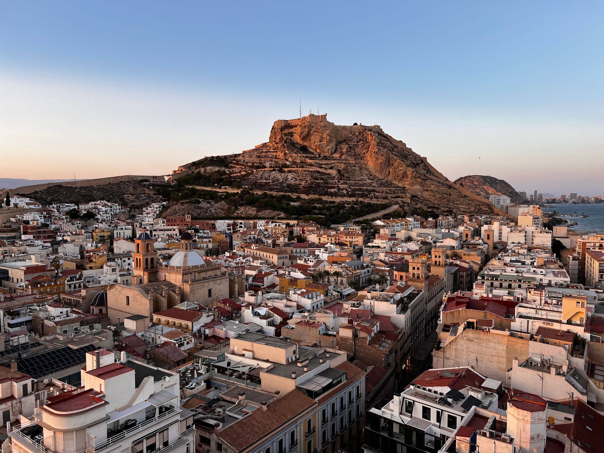 Santa Bárbara Castle on its hill above the rooftops of Alicante's old town at dusk.