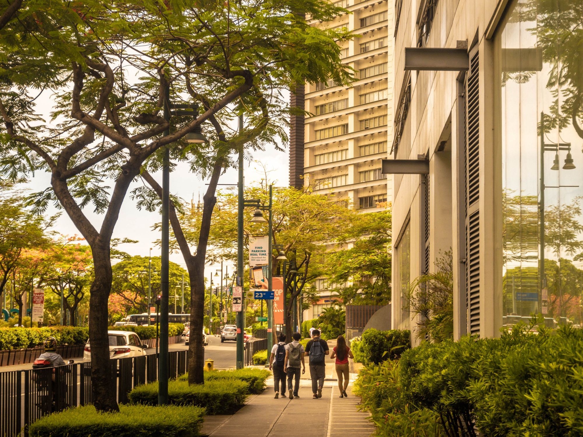 People walking along a tree-lined sidewalk beside high-rise buildings in Bonifacio Global City in Taguig.