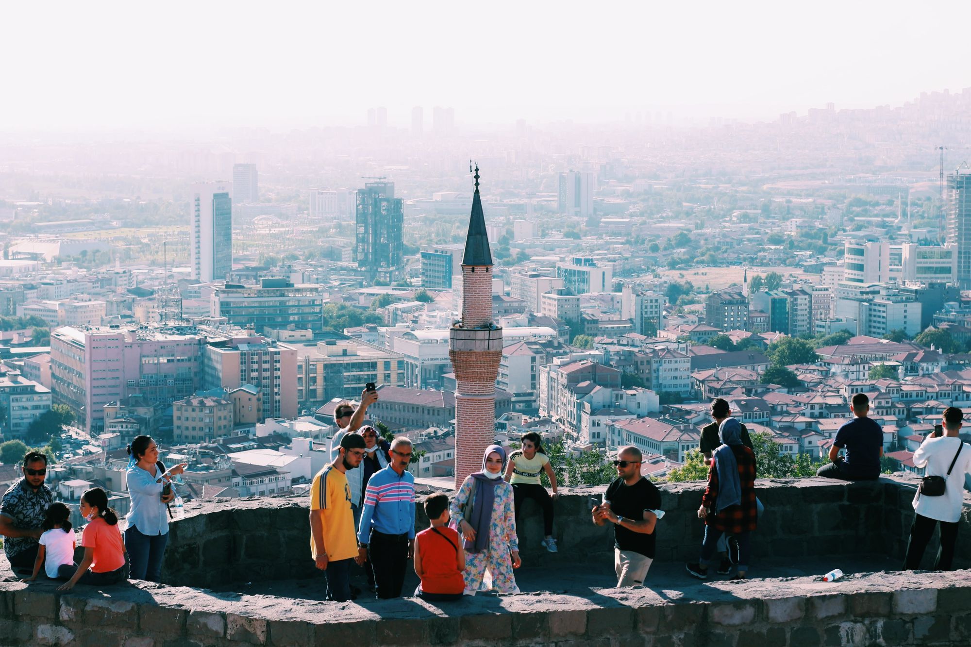 The Ankara skyline with a minaret, seen from the wall of the castle viewpoint with visitors along it.