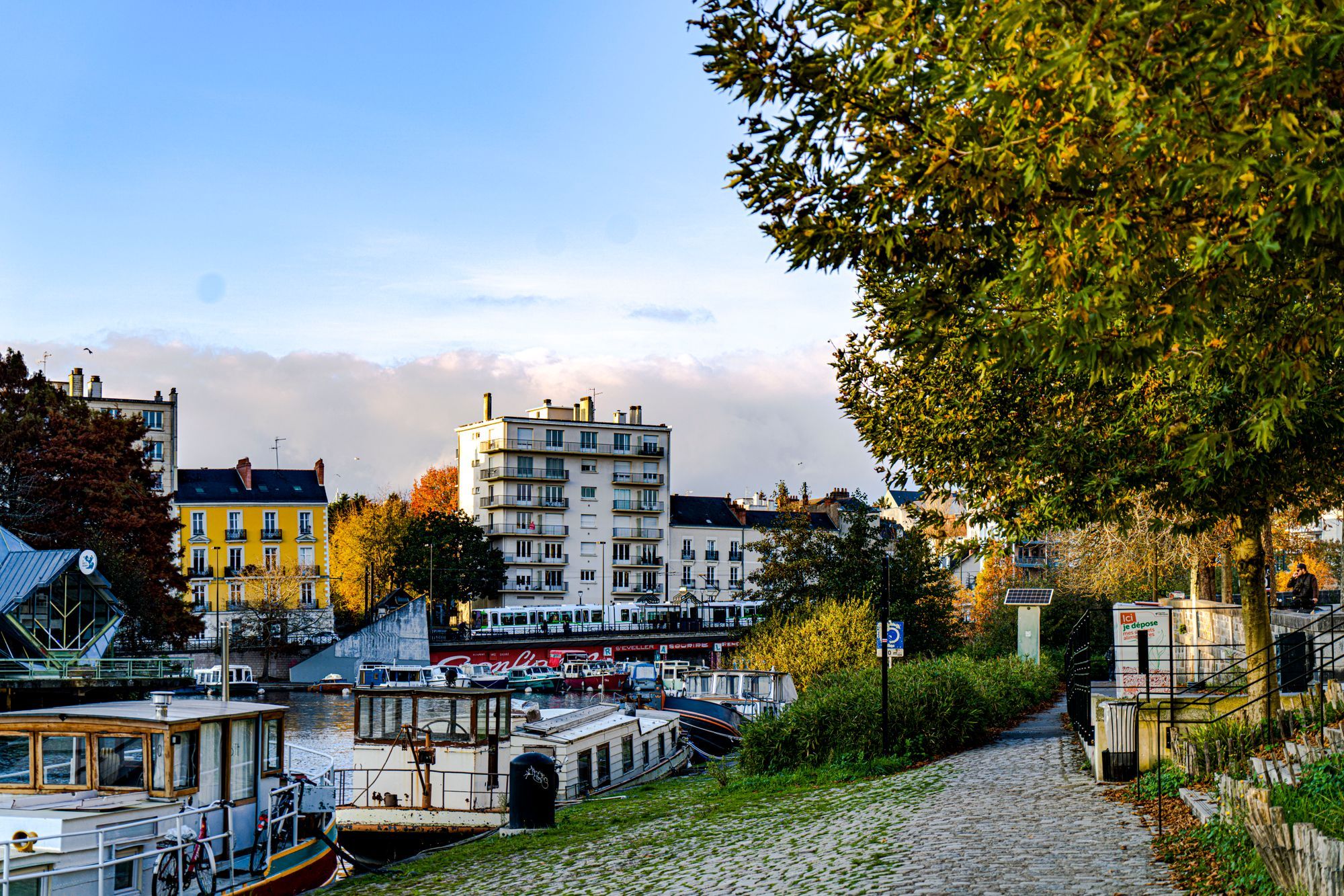 A riverside path with moored boats and apartment buildings in Nantes.