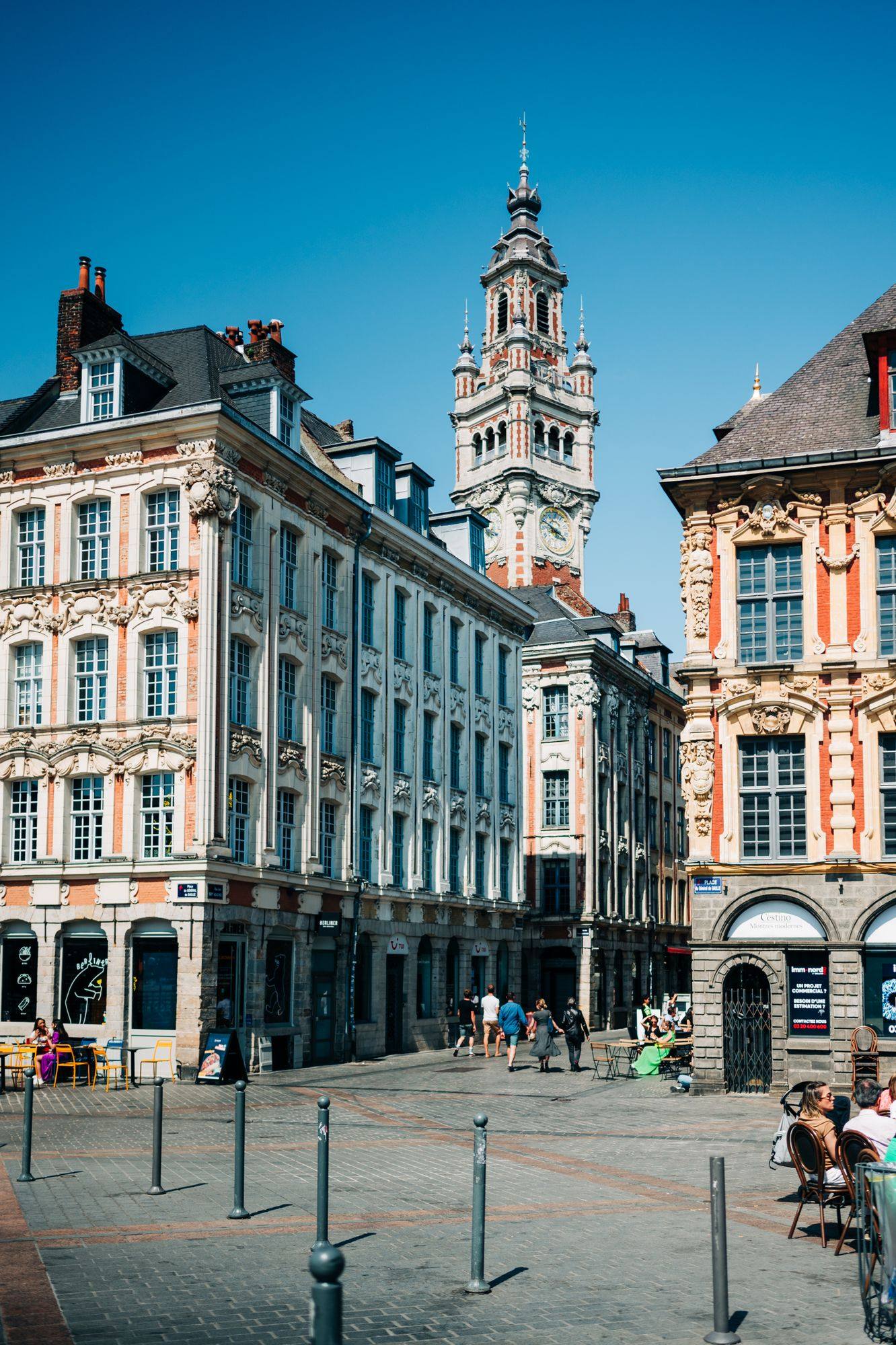 The belfry of the Chambre de Commerce above the Grand'Place in Lille, between ornate brick and stone facades under a blue sky.