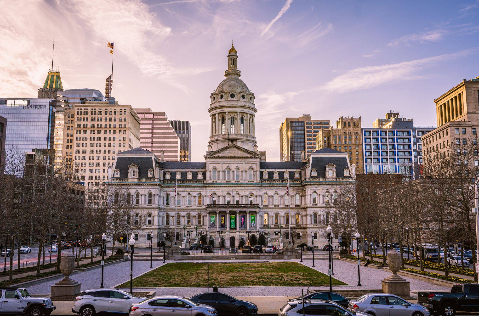 Baltimore City Hall with its dome and the downtown towers behind it at dusk.