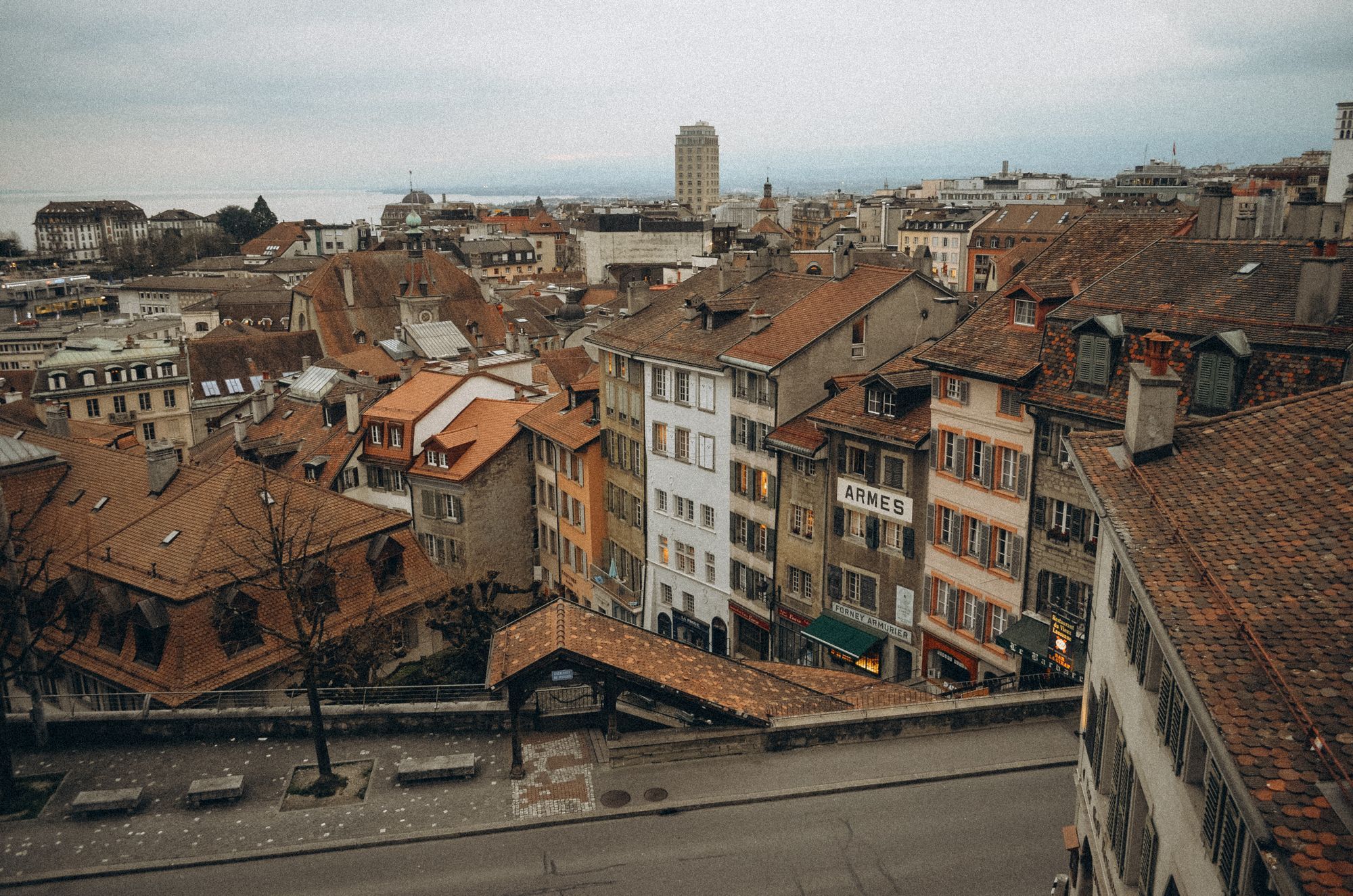 The tiled rooftops of Lausanne's old town, with the city and the lake haze beyond.