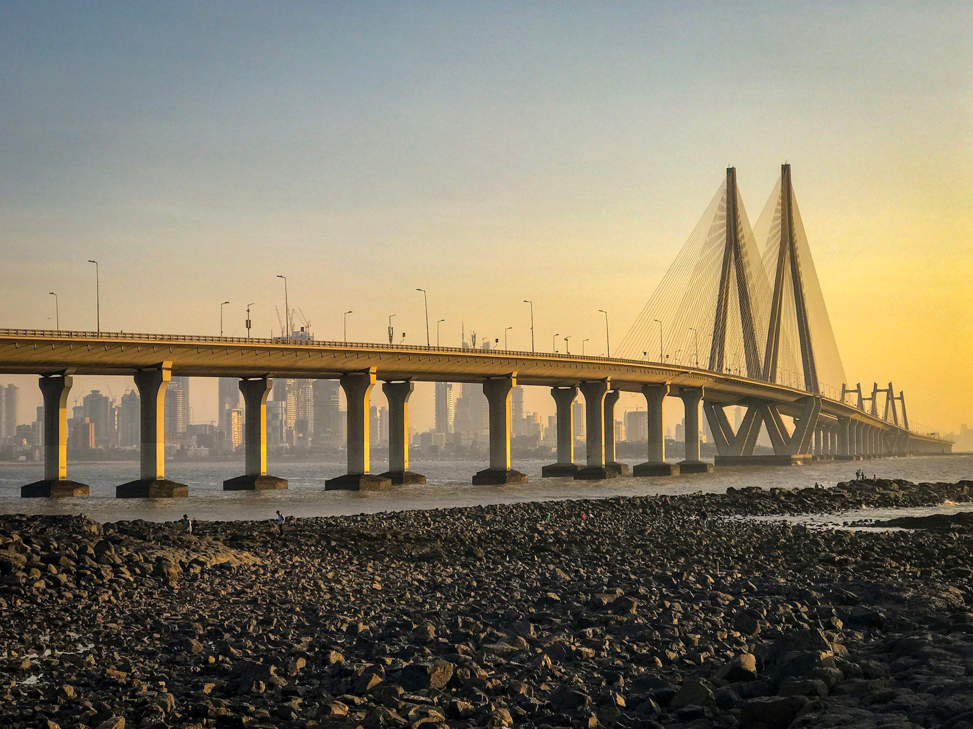 The Bandra-Worli Sea Link in Mumbai at golden hour, with its cable towers against a yellow sky and the city skyline behind the bridge.