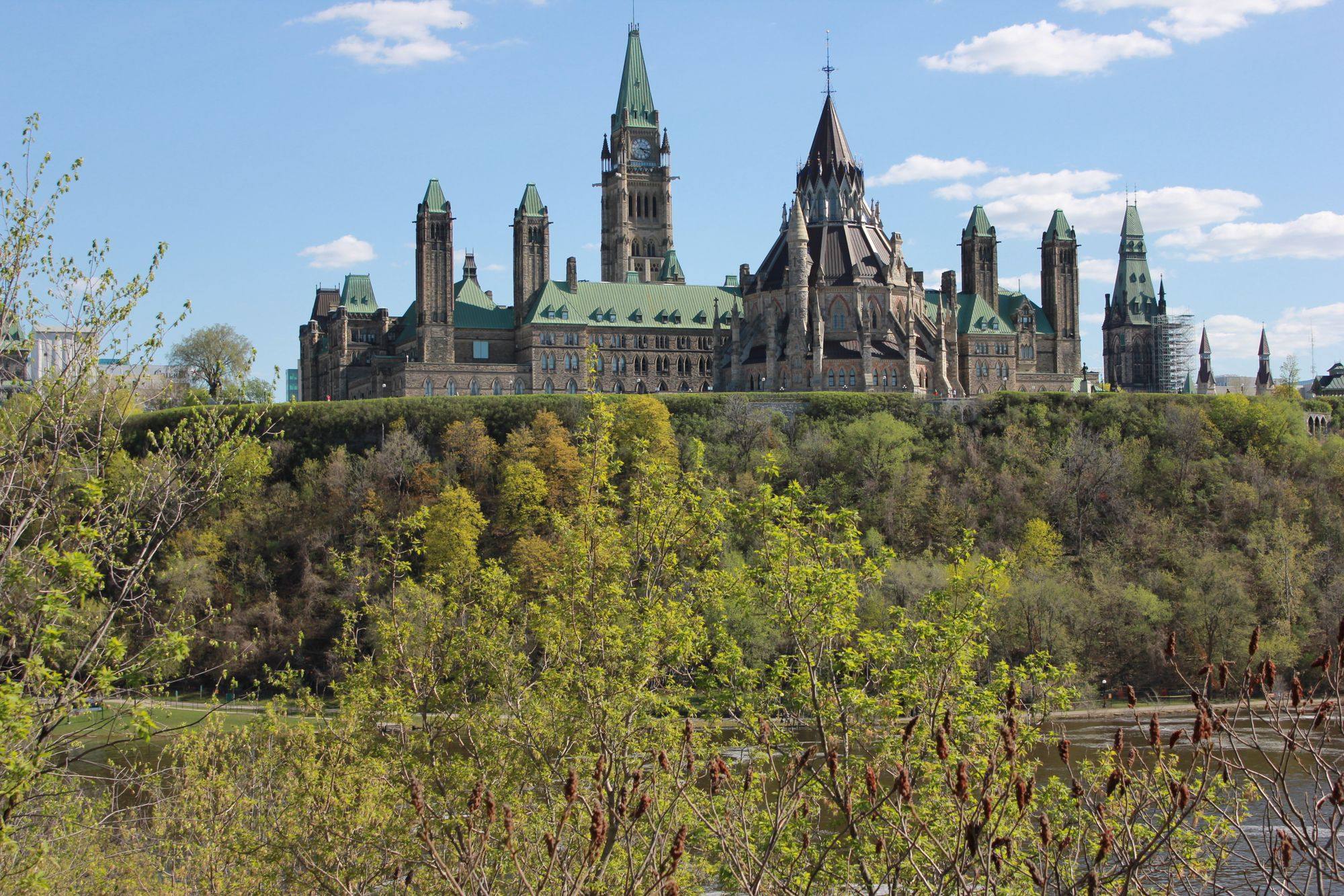 The Parliament Hill buildings above the wooded riverbank in Ottawa on a spring day.