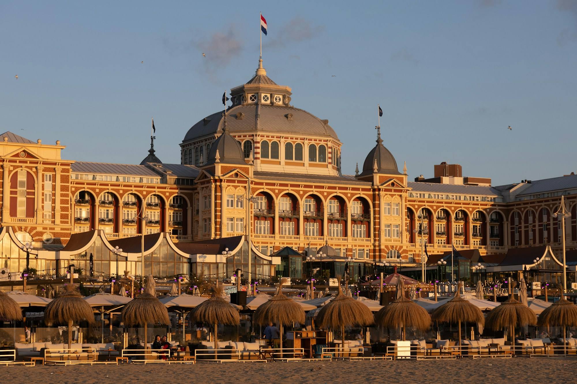 The domed Kurhaus on the seafront at Scheveningen in The Hague at sunset, with rows of beach umbrellas below.