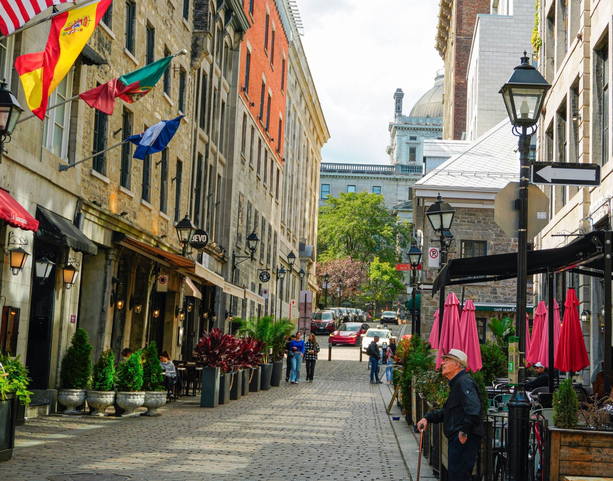 A cobblestone street in Old Montreal with café terraces and flags