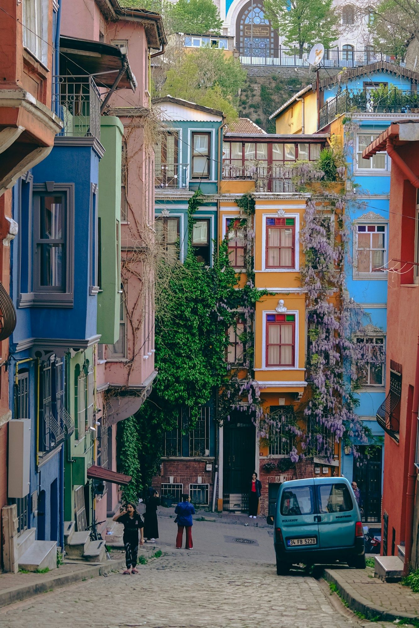 Colorful painted houses along a sloping cobbled street in Balat, Istanbul, with a few people walking.