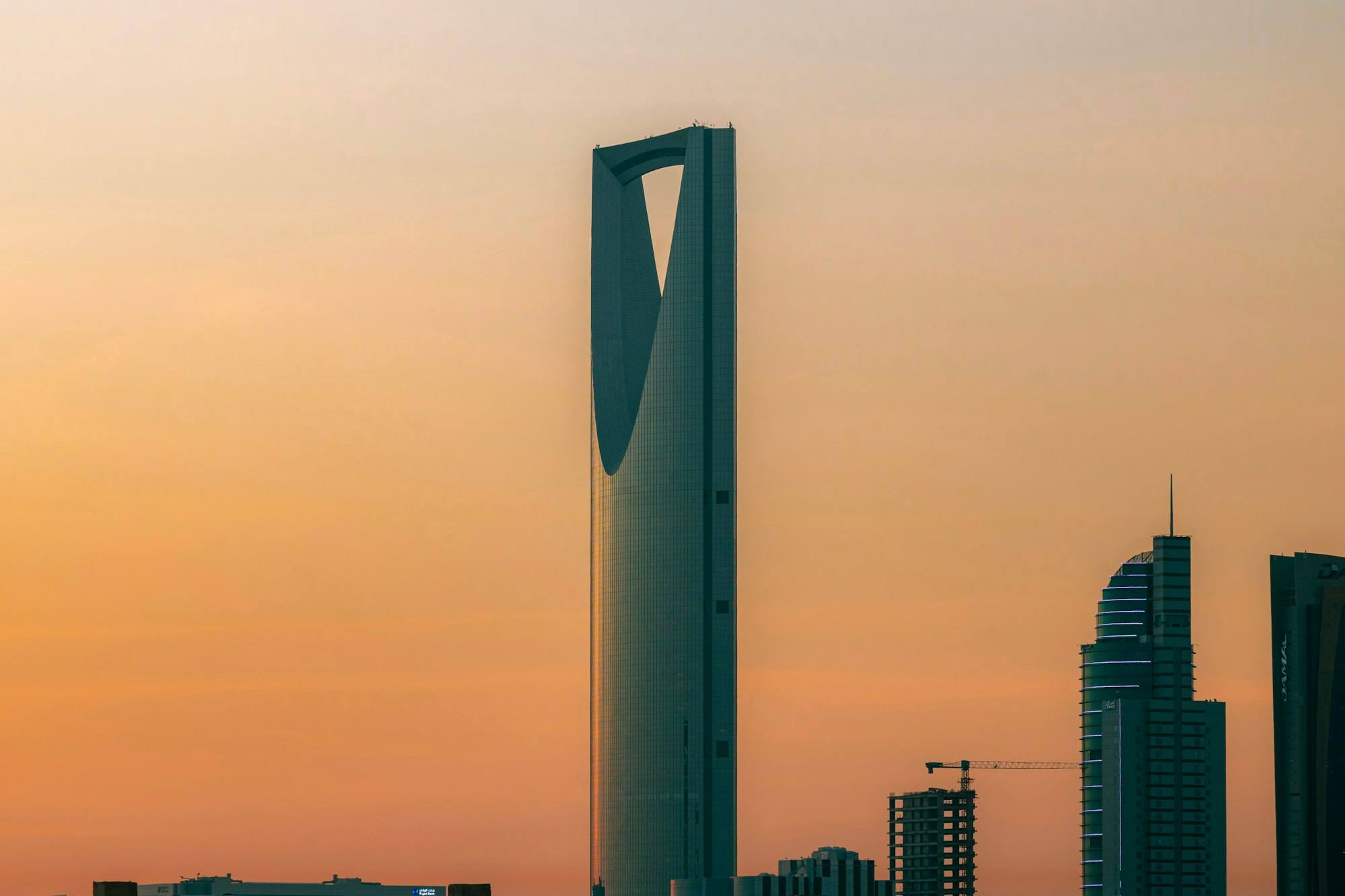 The Kingdom Centre tower in Riyadh at sunset, with the opening near its top against a warm orange sky.
