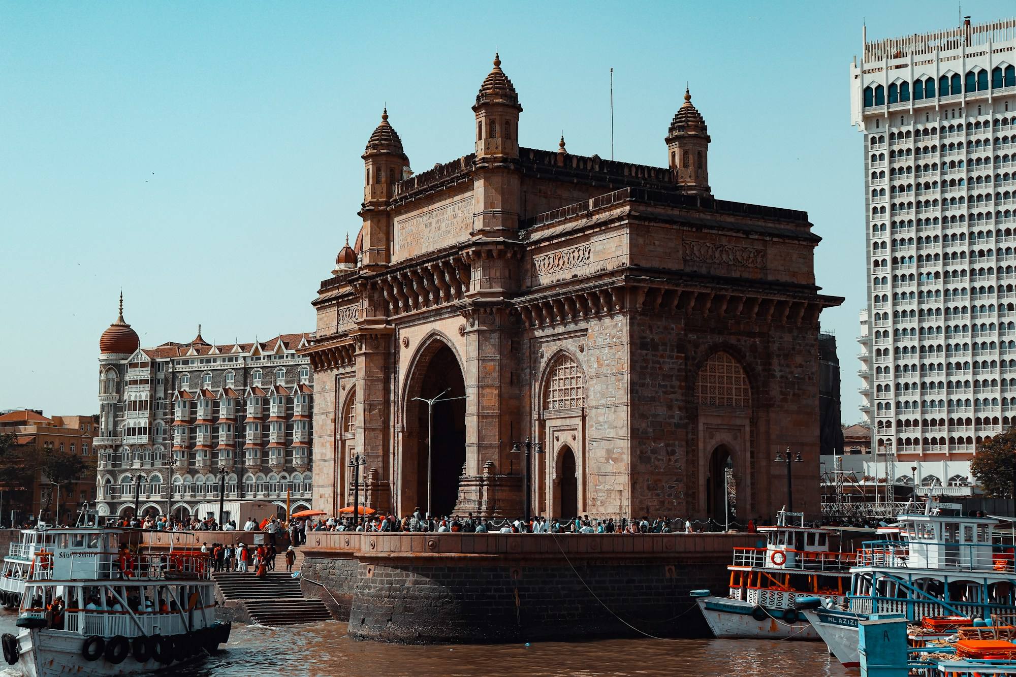 The Gateway of India on the Mumbai waterfront, with the Taj Mahal Palace hotel beside it and boats moored in front.