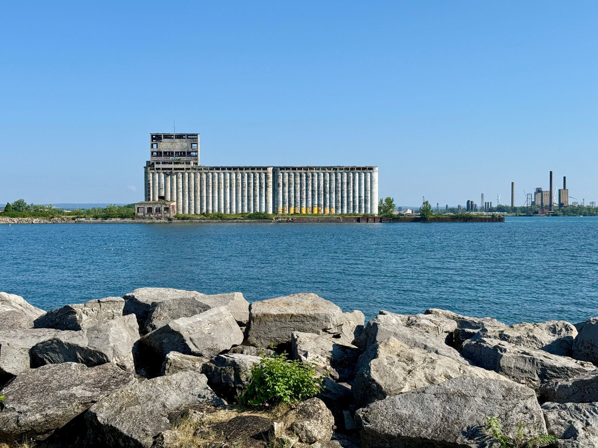 A grain elevator across the water on Lake Erie at Buffalo, with rocks in the foreground.