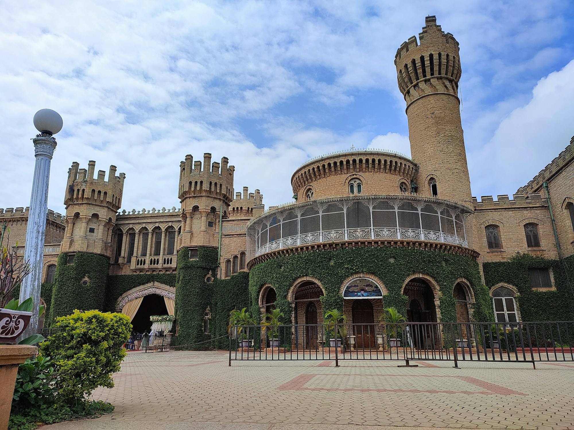 Bangalore Palace, with its round stone tower and ivy-covered walls, under a blue sky with clouds.