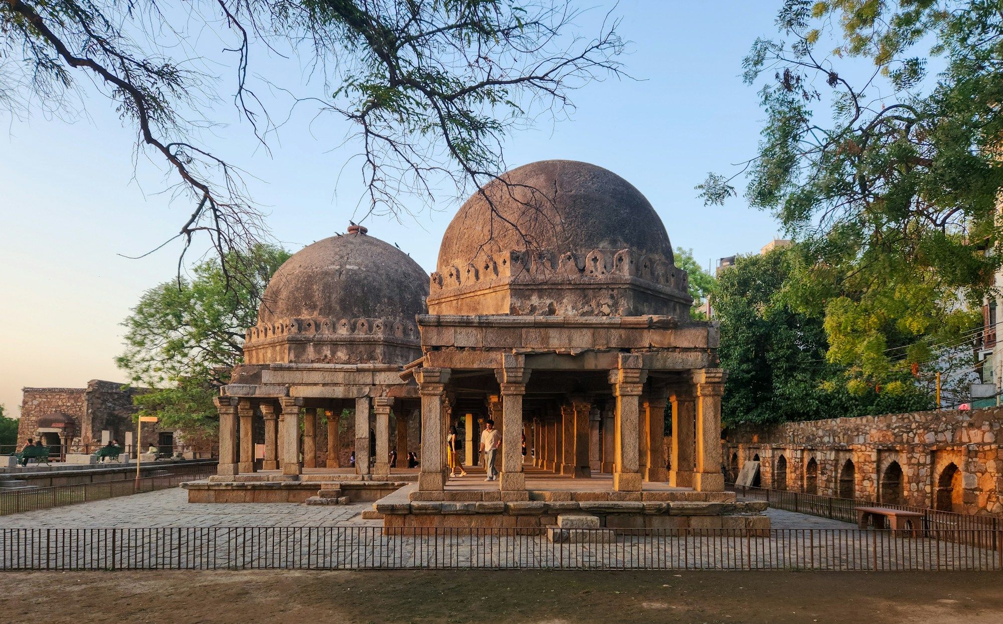 The domed tombs of the Hauz Khas complex in South Delhi, seen through tree branches under a blue sky.