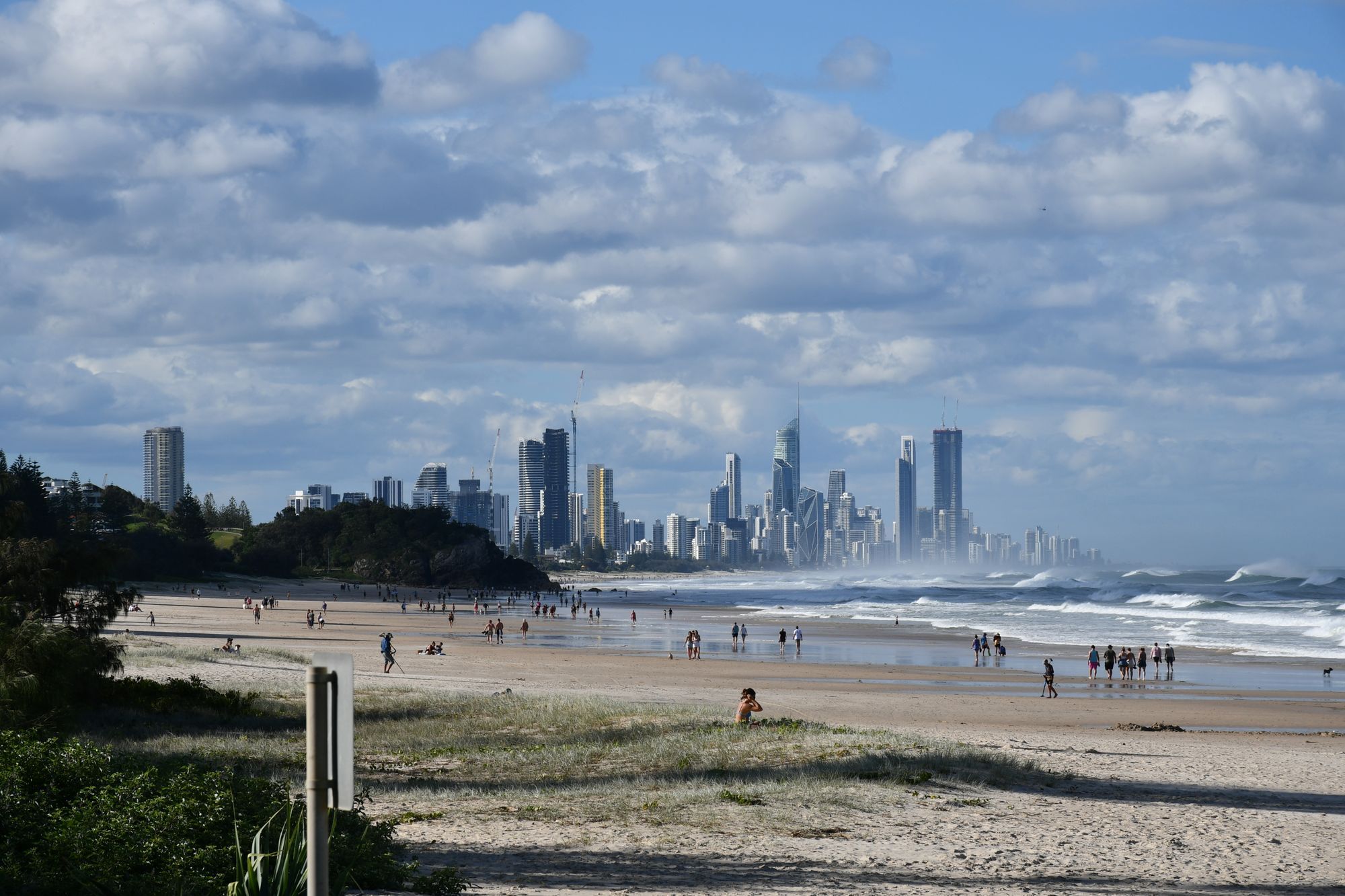 People walking along the beach on the Gold Coast, with the skyline in the distance under a cloudy sky.