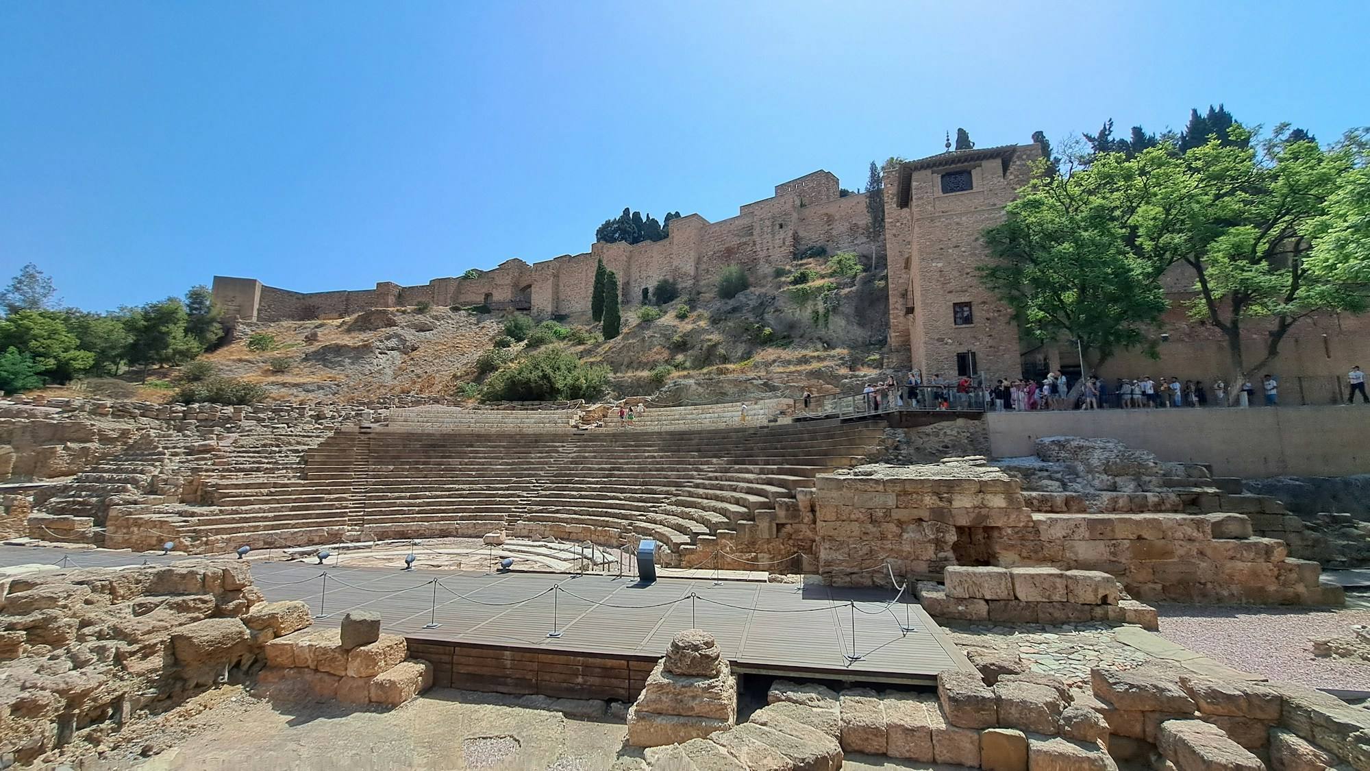 The walls of the Alcazaba of Málaga on the hillside above the Roman Theatre, under a blue sky.