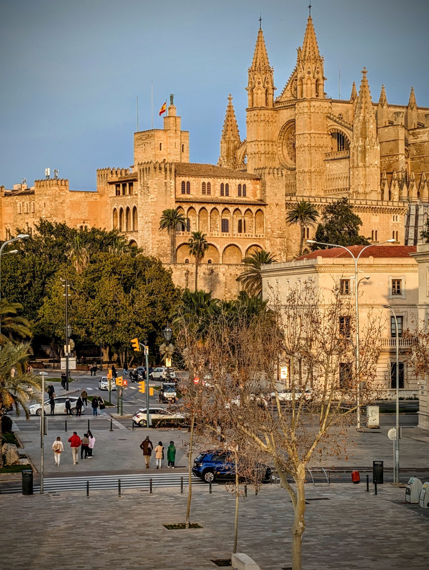 Pedestrians crossing a street below the Palma Cathedral and the Almudaina Palace in Palma de Mallorca.