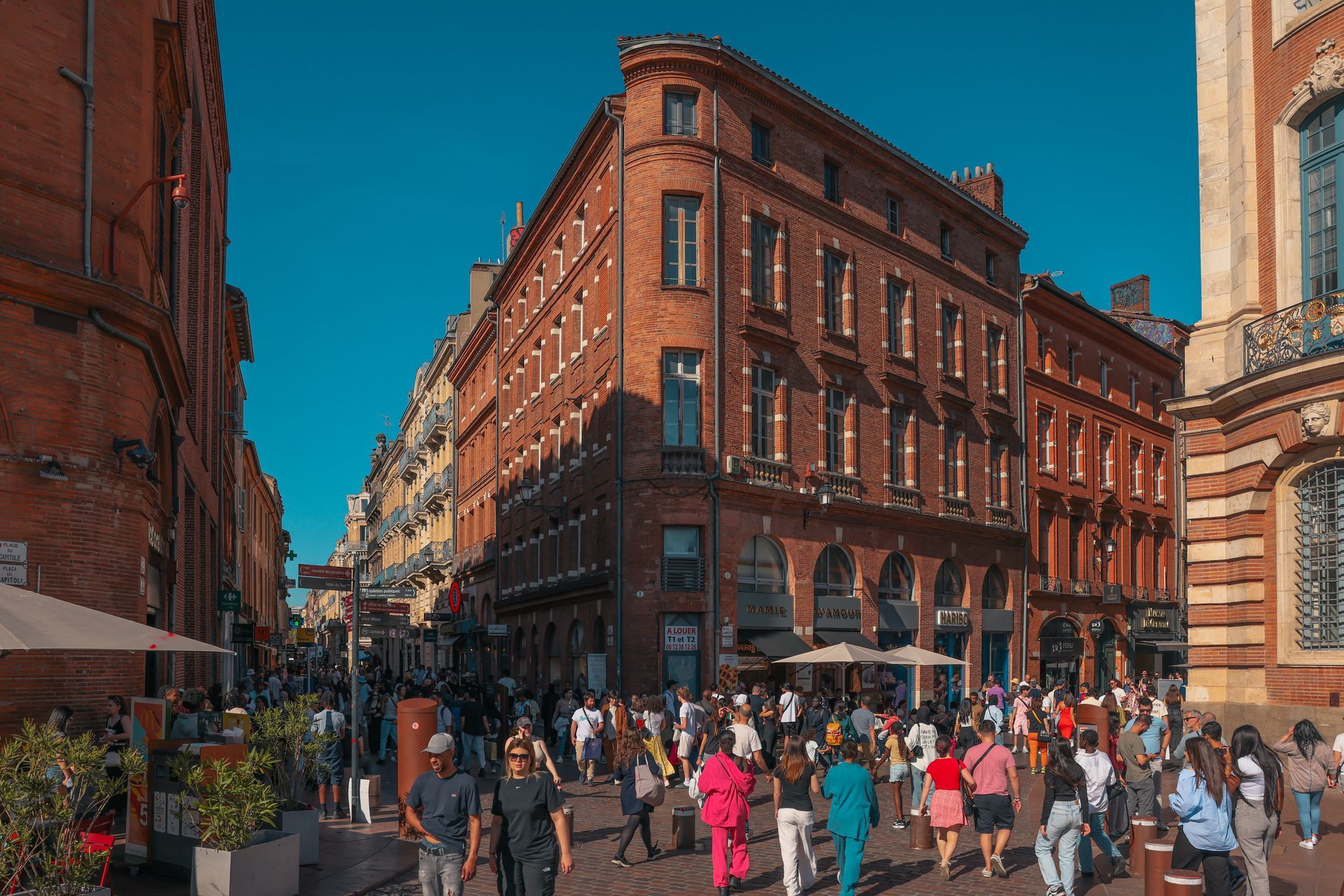 A busy pedestrian street lined with red-brick buildings in the historic center of Toulouse.