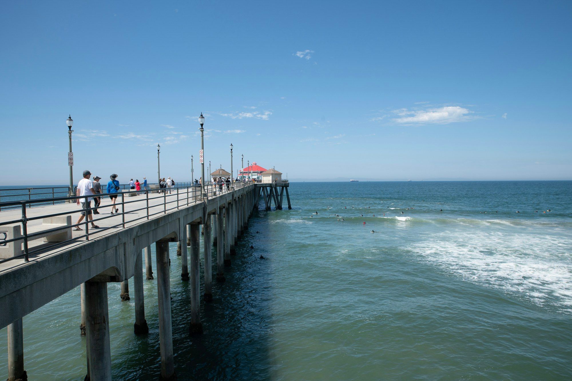People walking along Huntington Beach Pier on a sunny day, with the ocean below.