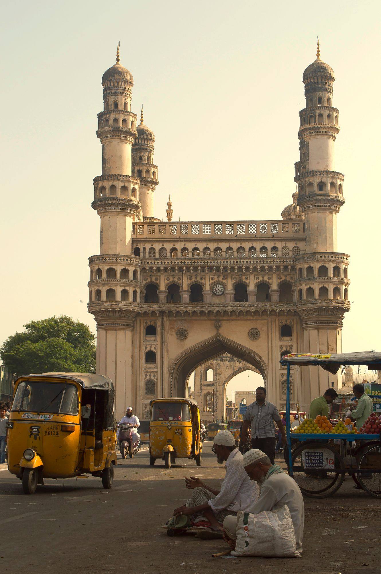 The Charminar in Hyderabad in warm evening light, with auto-rickshaws and people on the square in front.