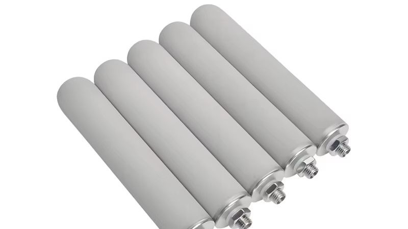 Rolls of stainless steel woven wire mesh and a cylindrical sintered filter cartridge on a factory workbench