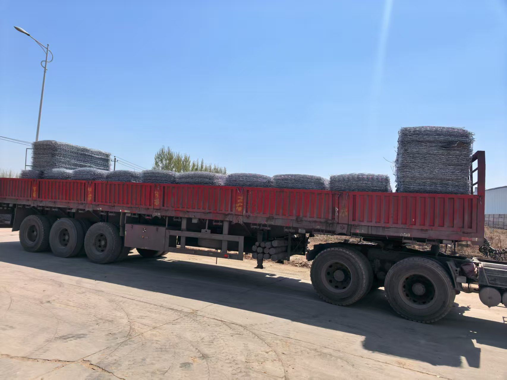 Flatbed truck loaded with wrapped wire mesh rolls leaving the factory