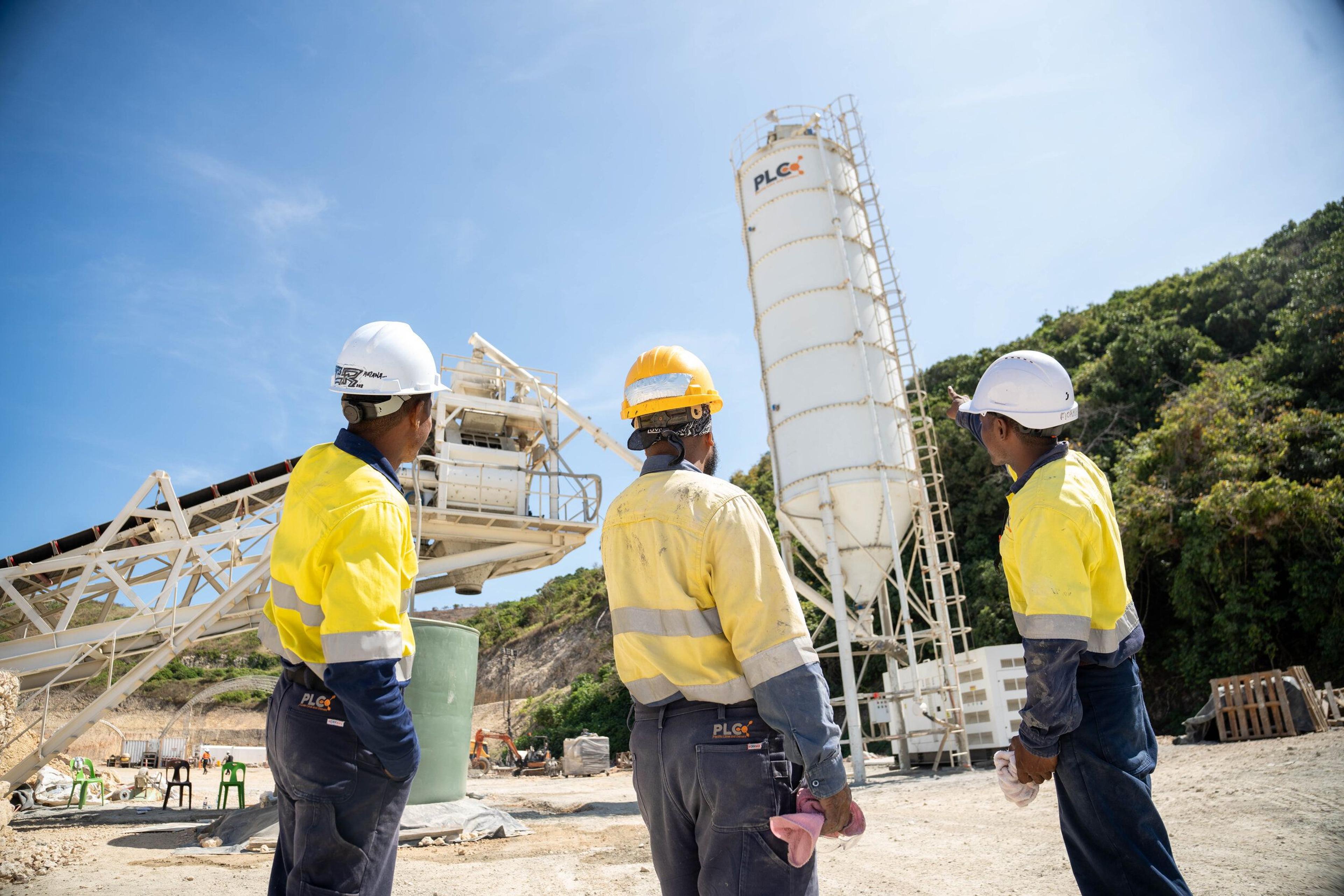 Three Pacific Lime and Cement workers in high visibility gear talking at the batch plant