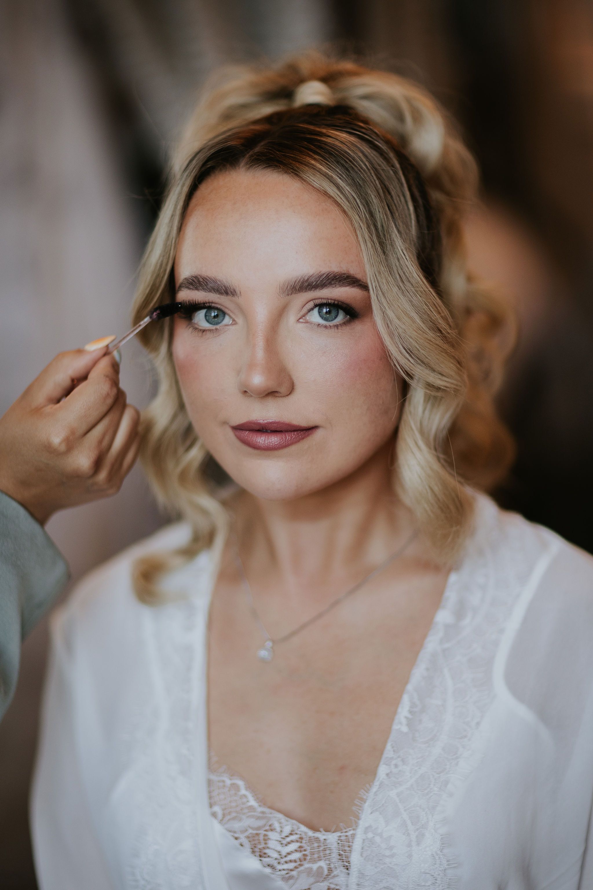 bride looking at the camera while mua applies mascara