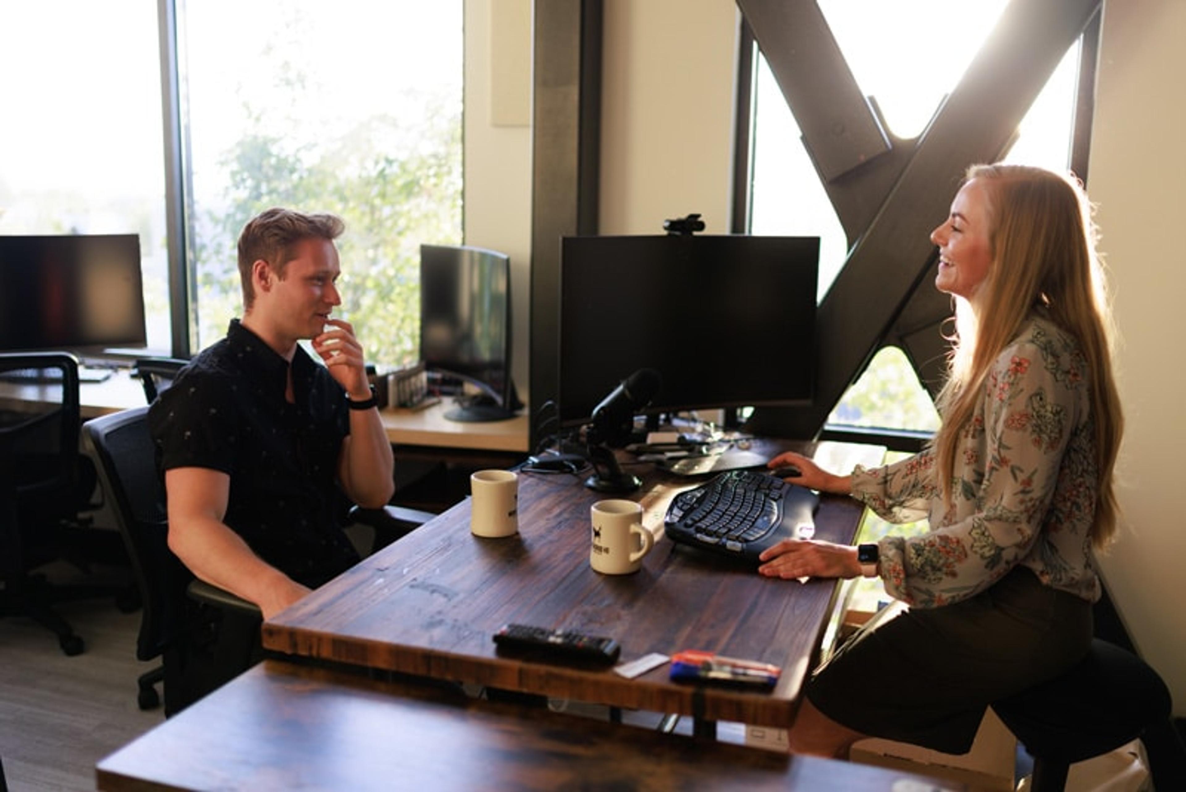 Two people chatting at a desk in a small office space in Edmonds at Workhorse Coworking