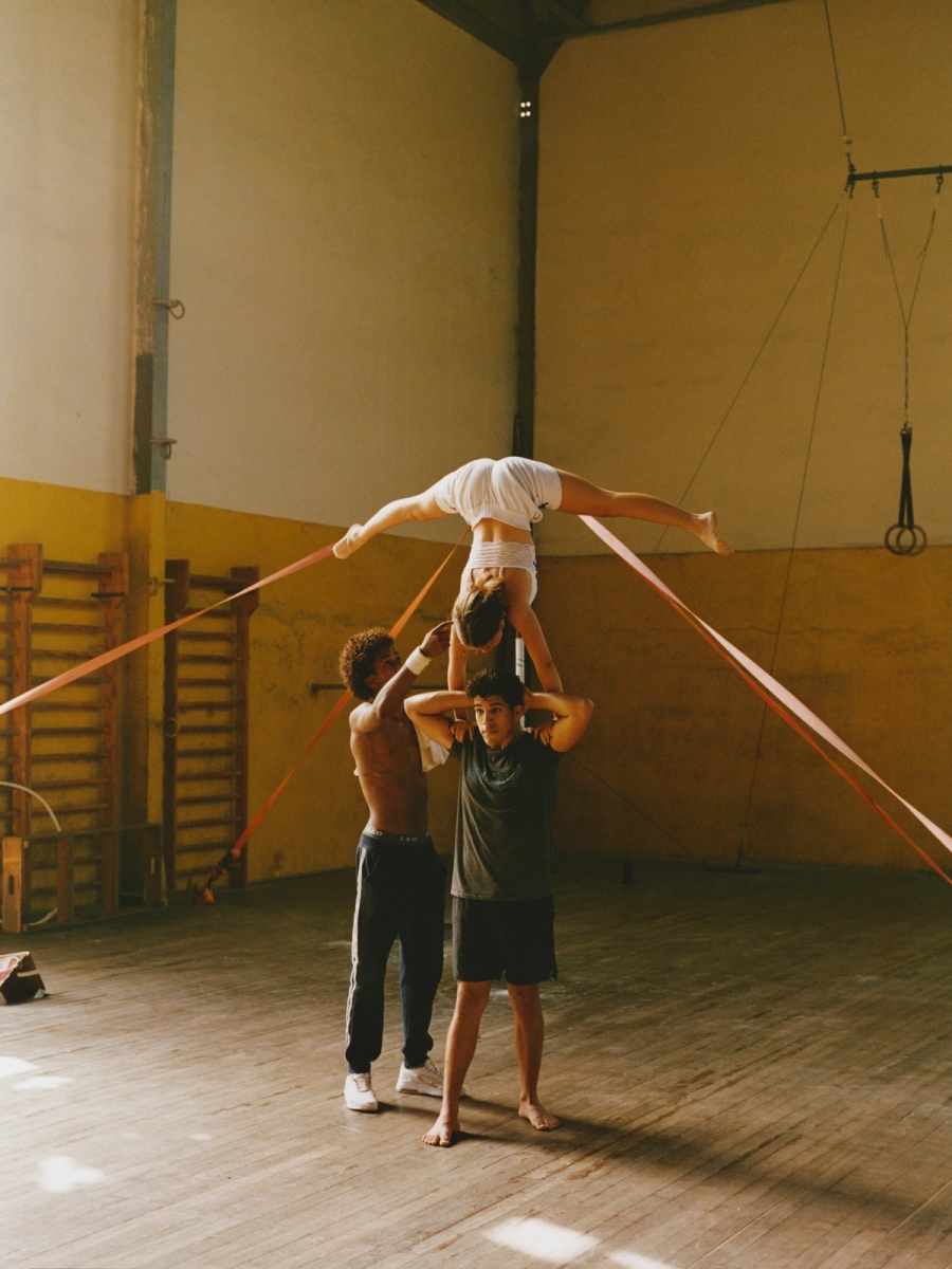 Left to right: Israel Ignacio Olivares Méndez and Yosdanis Font Crespo assist in lifting Amanda Boggiano Pardo during a balancing routine rehearsal. | Damian Dinza González performs an acrobatic routine on a suspended pole
