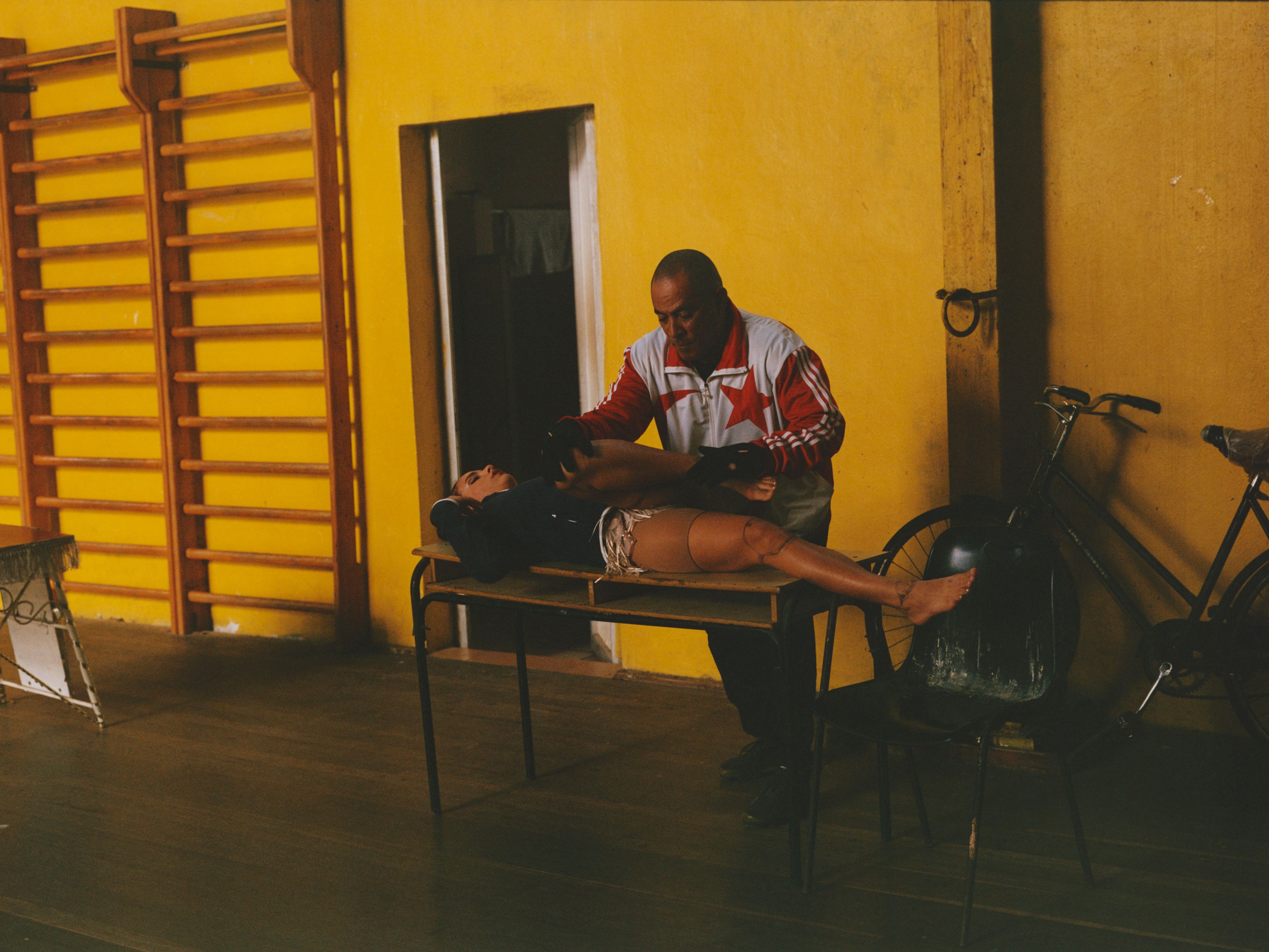 Naily De La Caridad Ortíz López is stretched by Professor Jorge Serguei Serguera before her aerial routine, highlighting the importance of flexibility and preparation in the circus arts.
