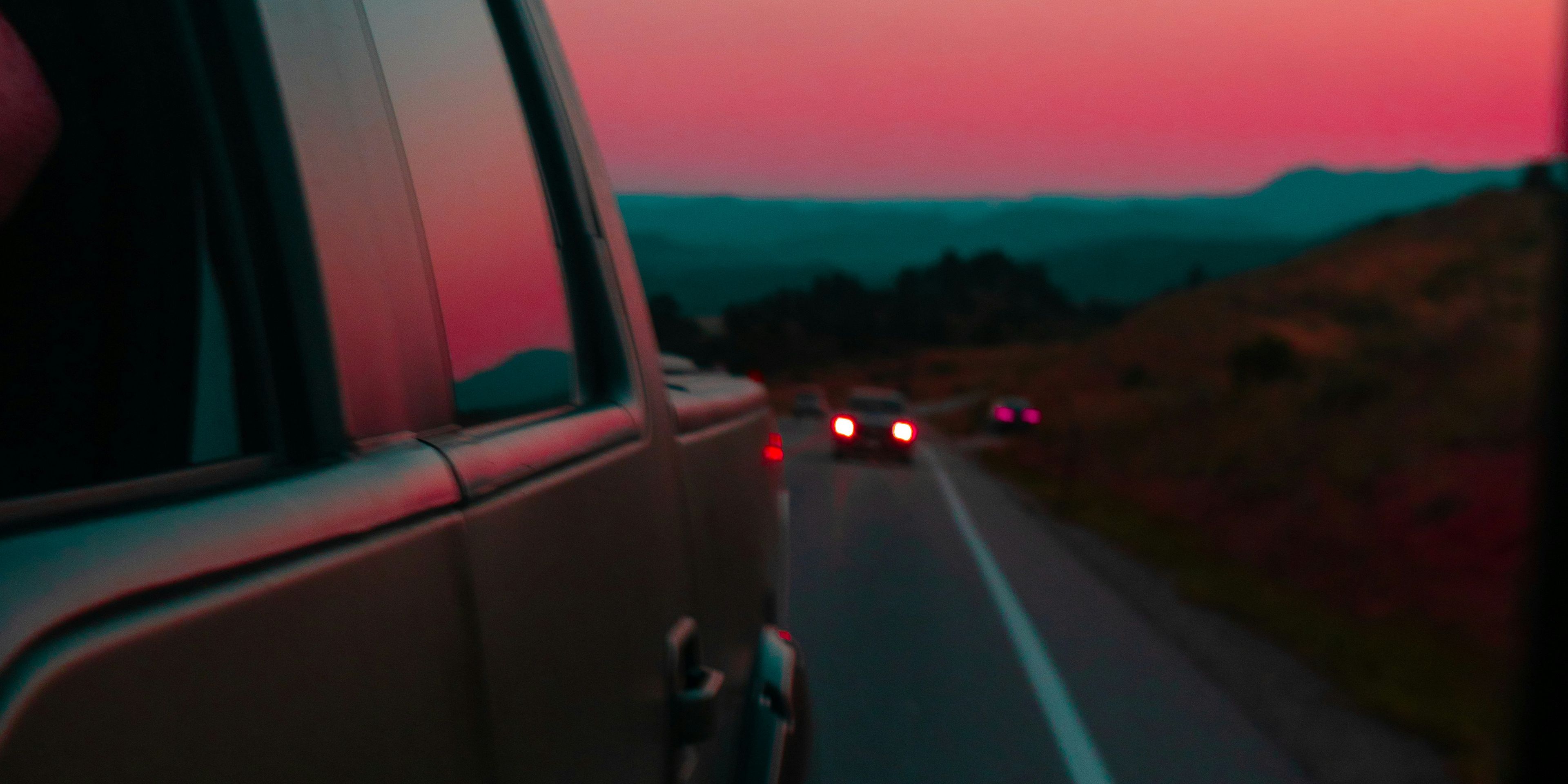 a car is driving down a road with a sunset in the background