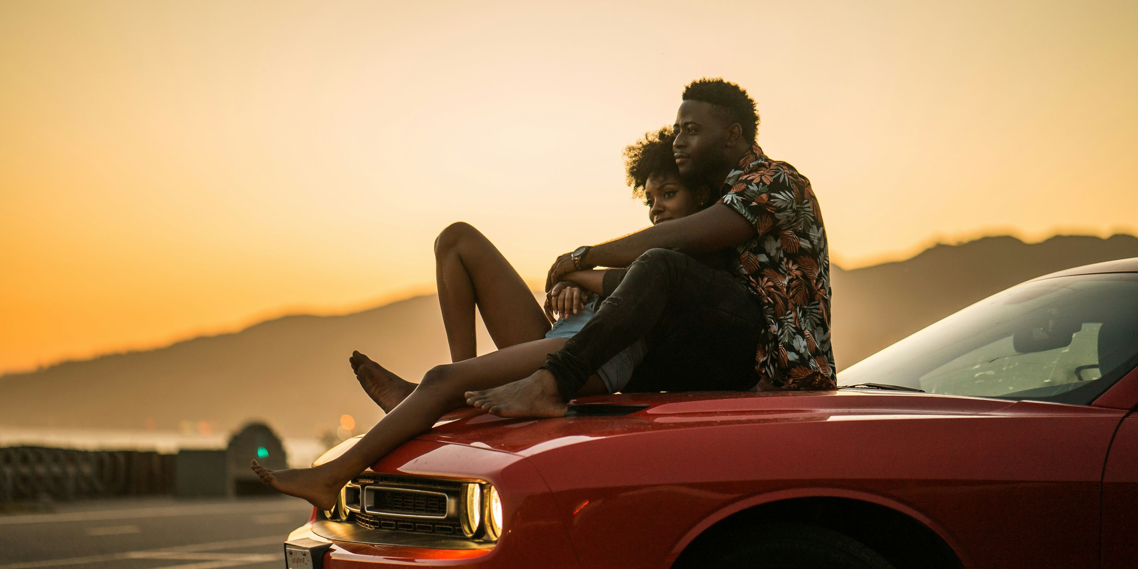 a man and a woman are sitting on the hood of a red car .