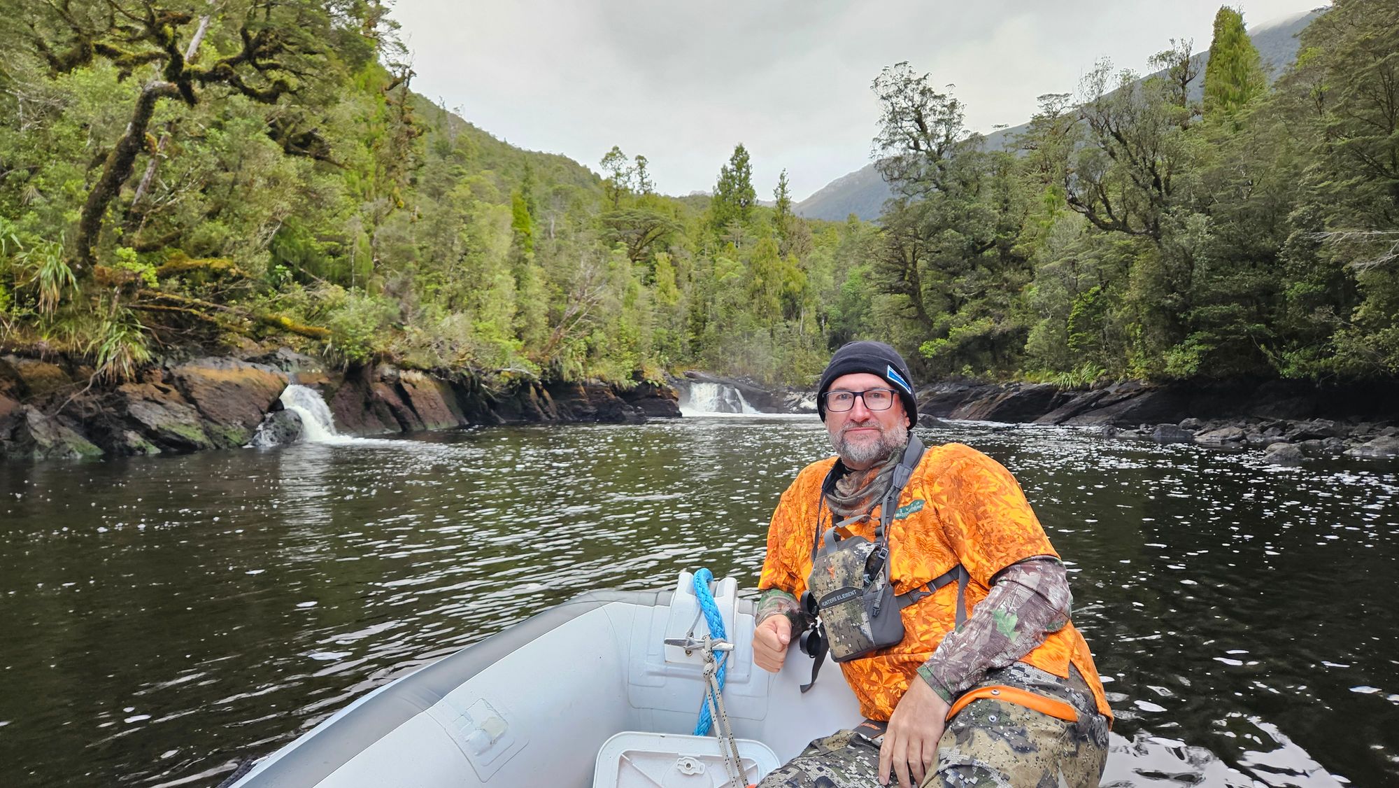 Crew member in camo and orange vest in the tender approaching cascading waterfalls at the head of Lake Cove river