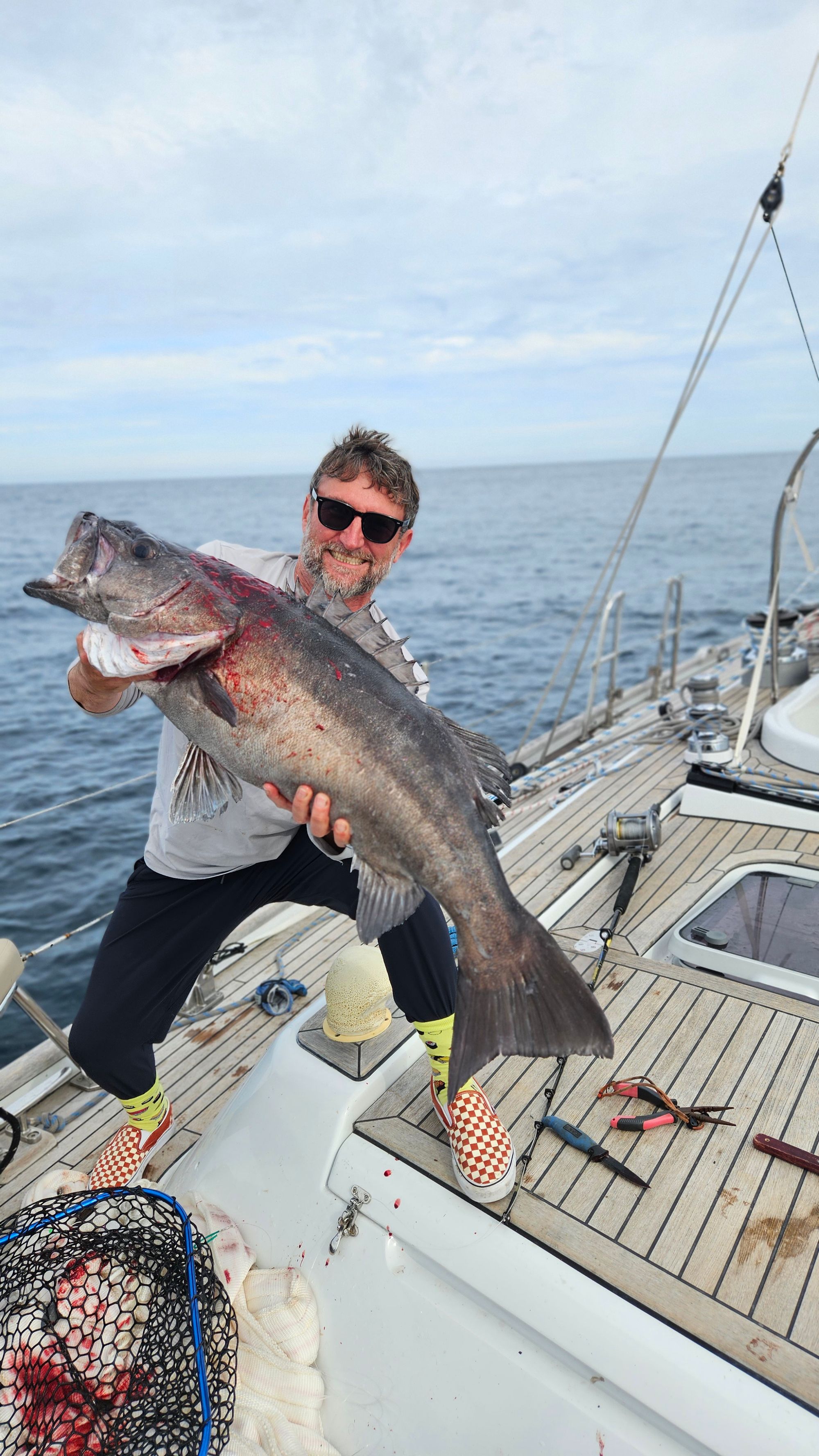 Crew member holding an enormous hapuku groper on Matariki III's deck, grinning, Chalky Inlet behind