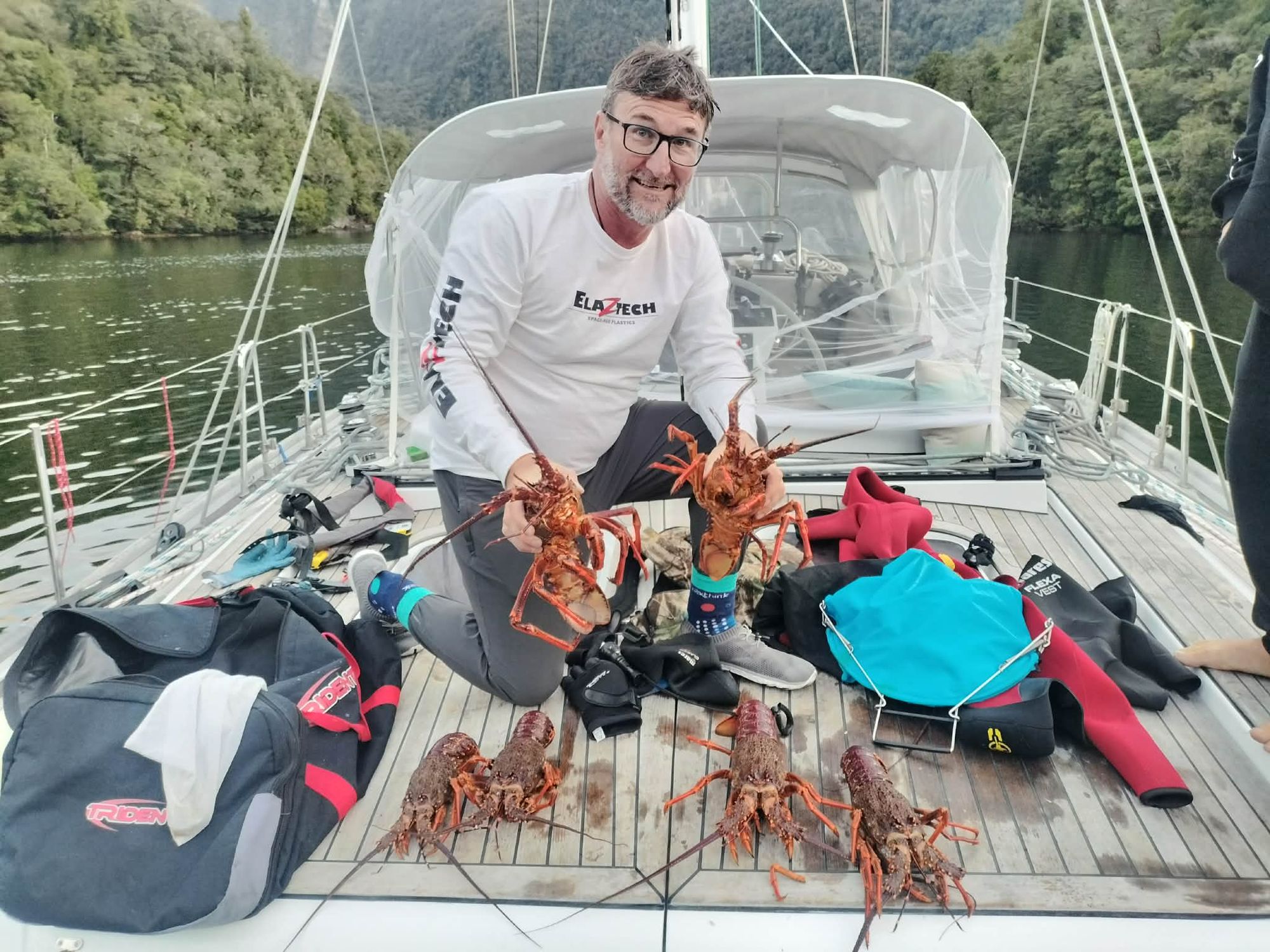 Crew member holding up two large crayfish on Matariki III's deck in Dusky Sound